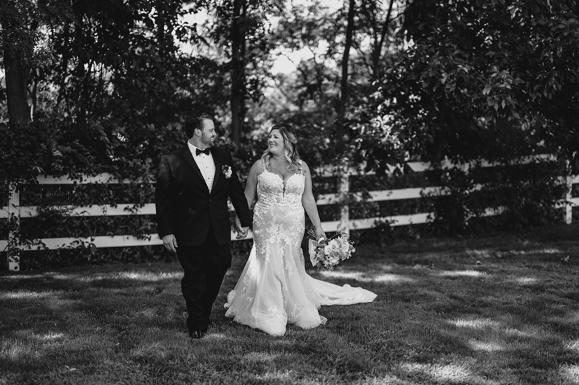 bride and groom hold hands walking away from white fence in yard of NJ venue