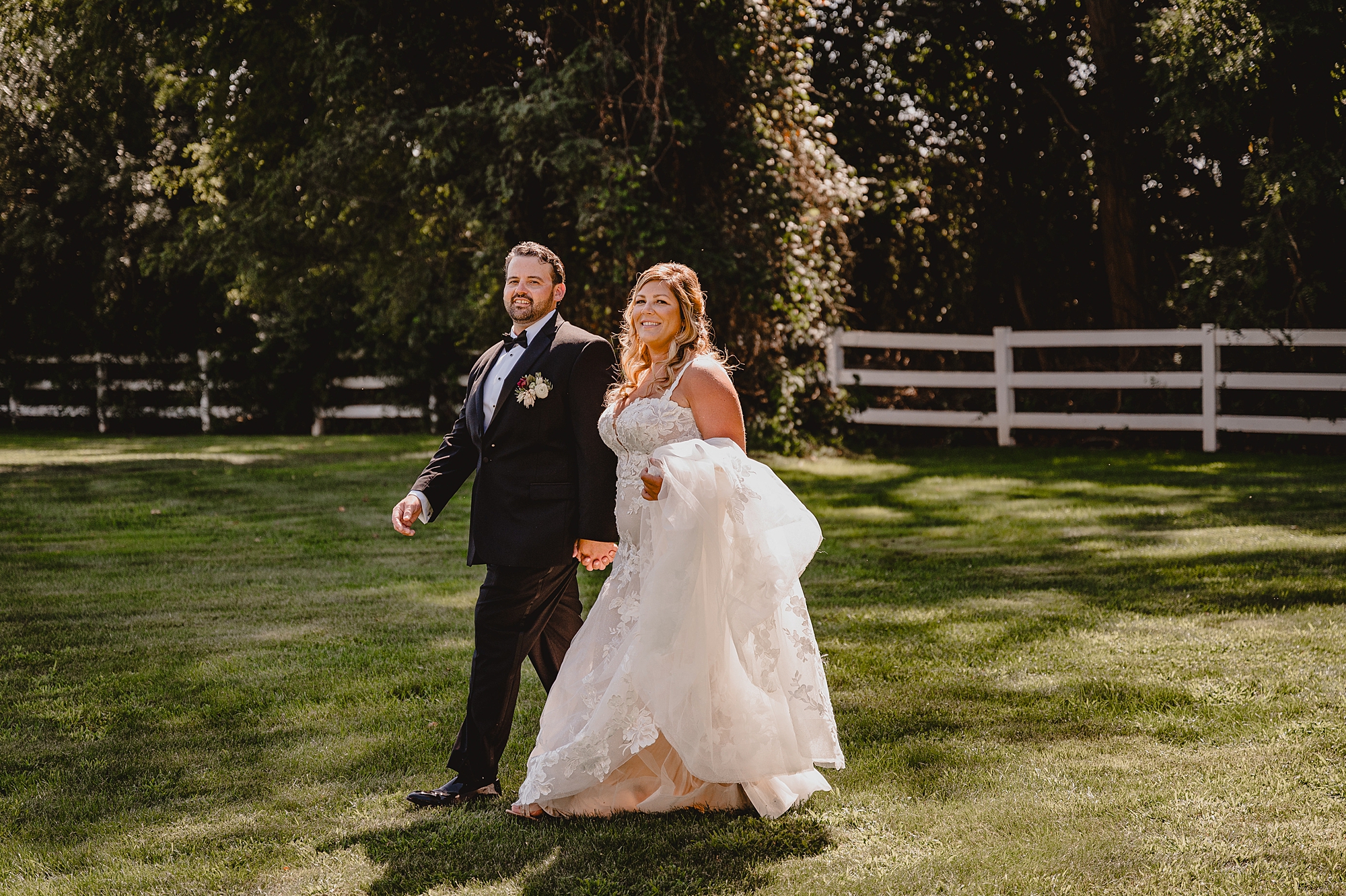 newlyweds walk on lawn near white fence at the Mill Lakeside Manor