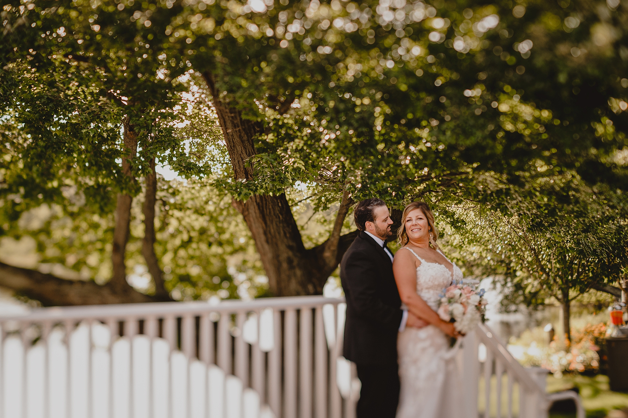 groom hugs bride from behind on edge of patio with white railing