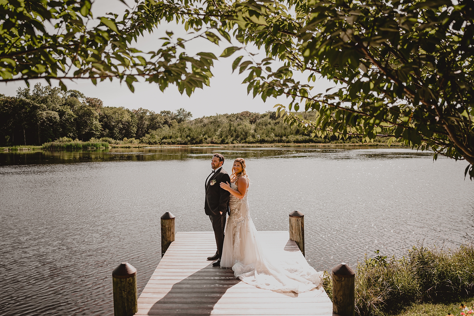 newlyweds stand on dock near pond at the Mill Lakeside Manor