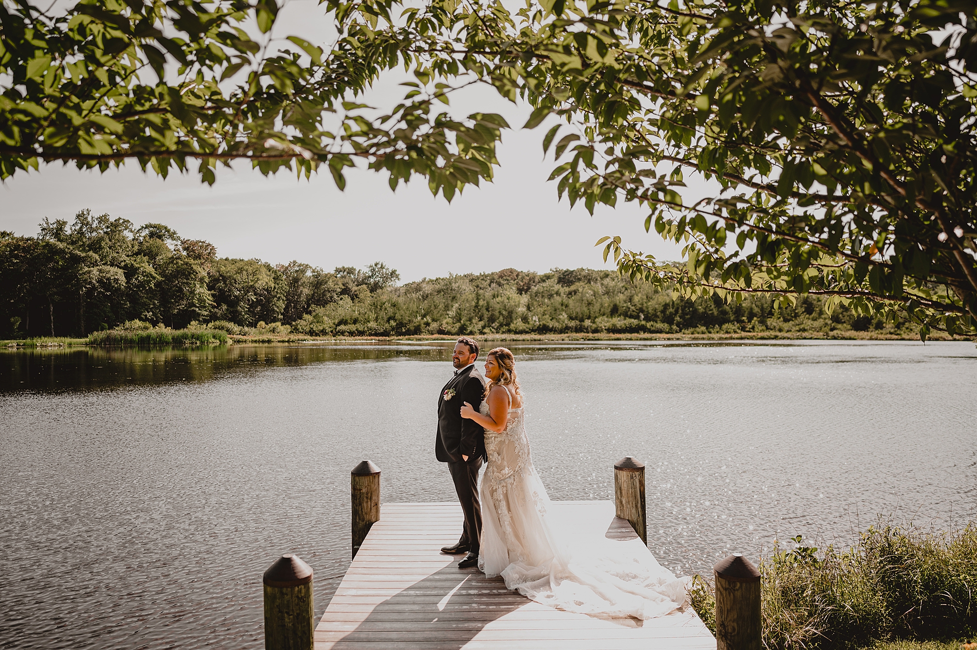 bride hugs groom from behind on dock at the Mill Lakeside Manor