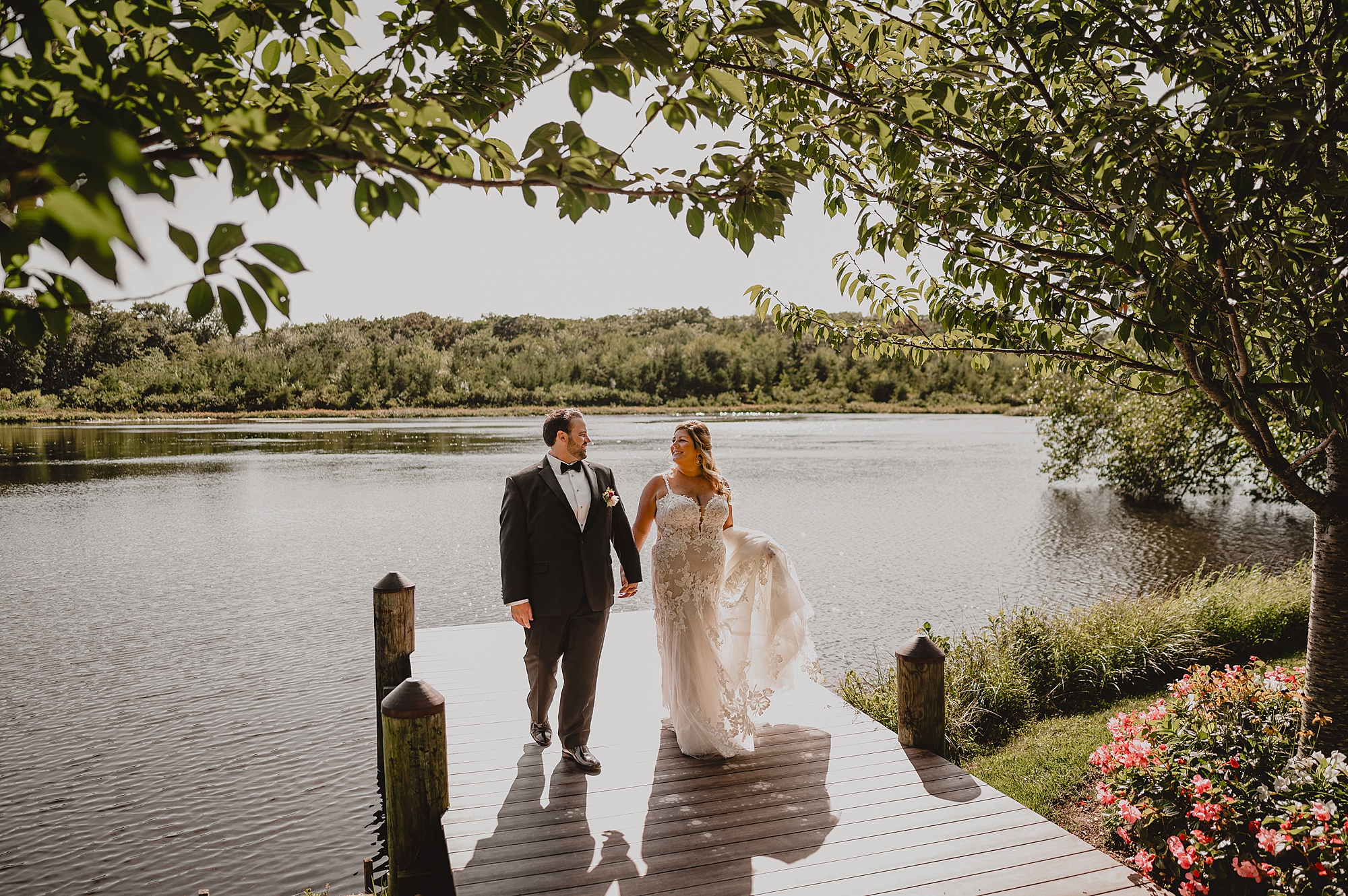 newlyweds hold hands walking on wooden dock at the Mill Lakeside Manor