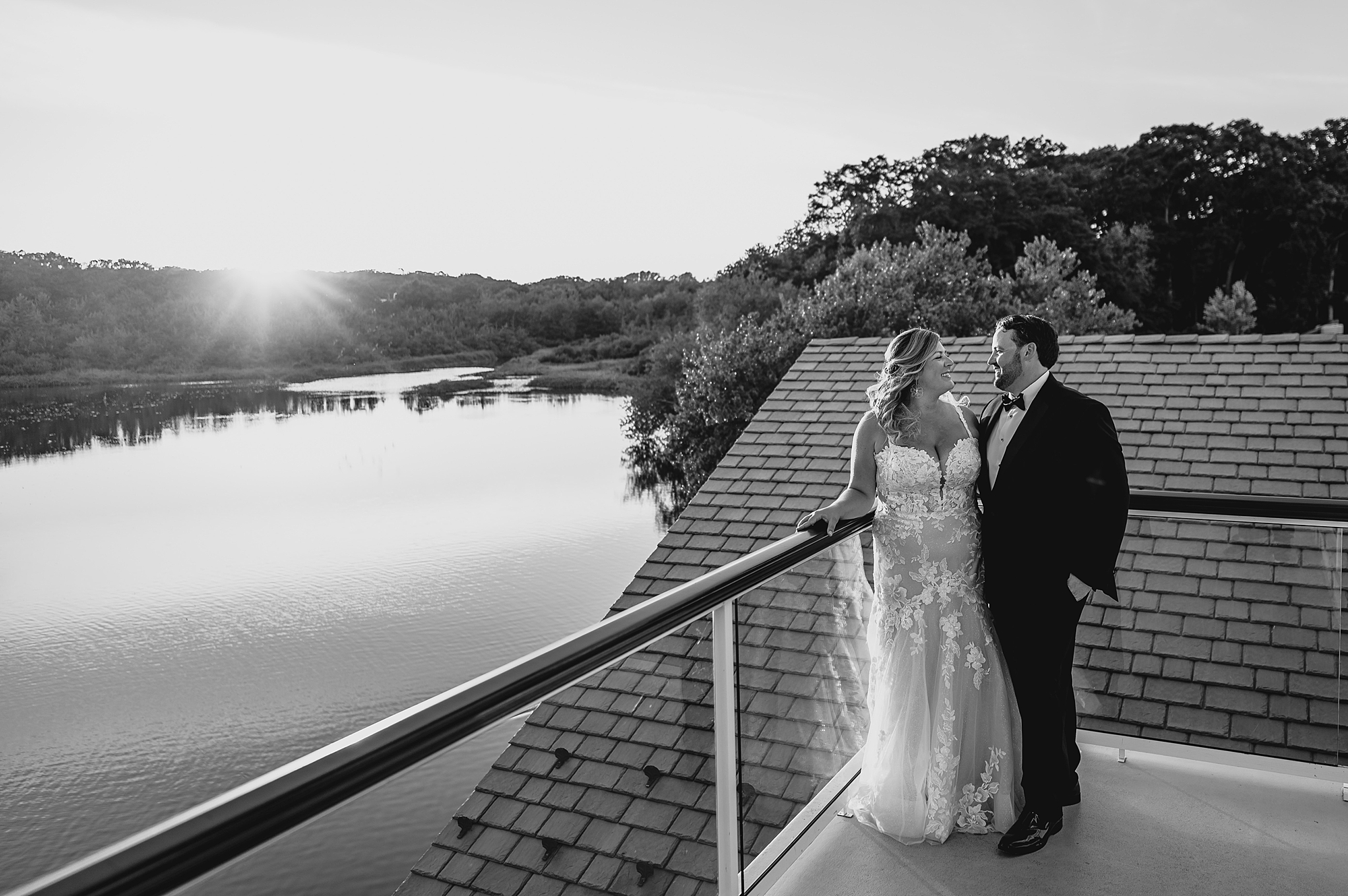bride and groom hug on balcony overlooking pond in New Jersey
