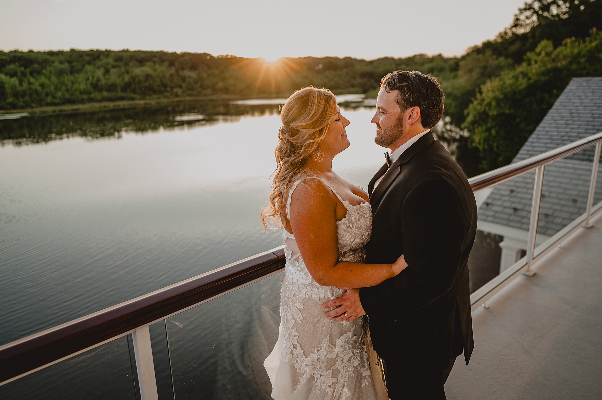 newlyweds hug at sunset on balcony overlooking pond at the Mill Lakeside Manor
