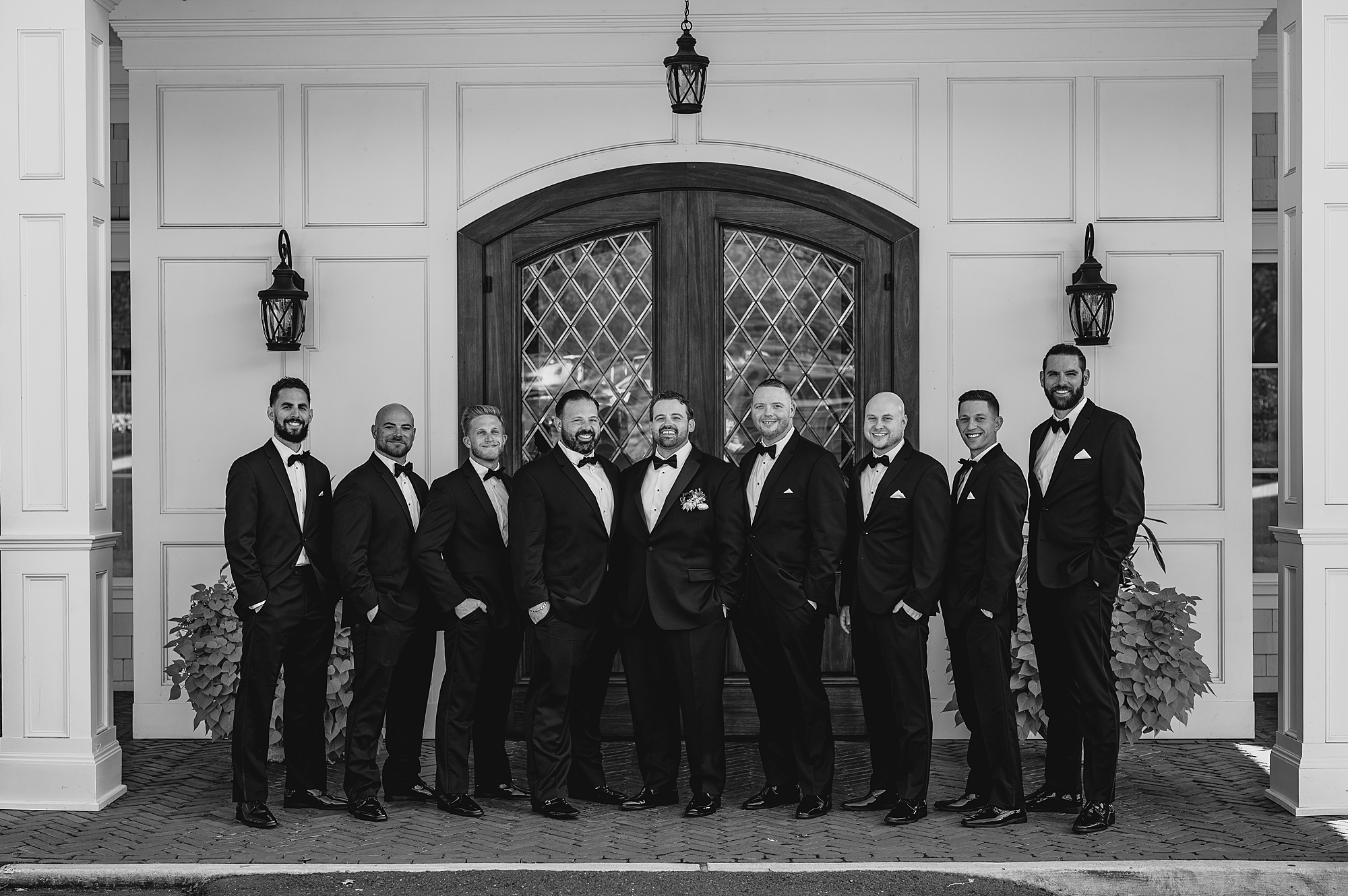 groom stands with groomsmen in black suits outside the Mill Lakeside Manor