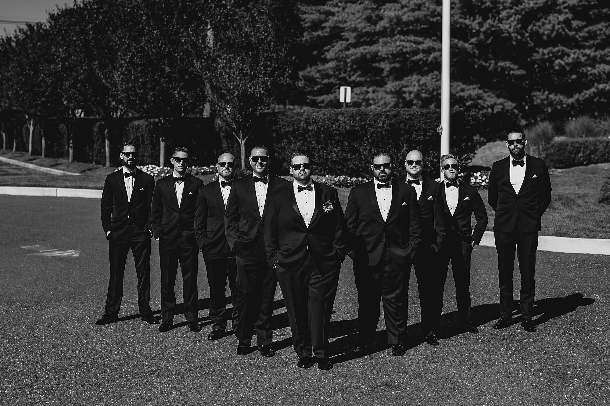 groom stands with groomsmen in V formation in black suits