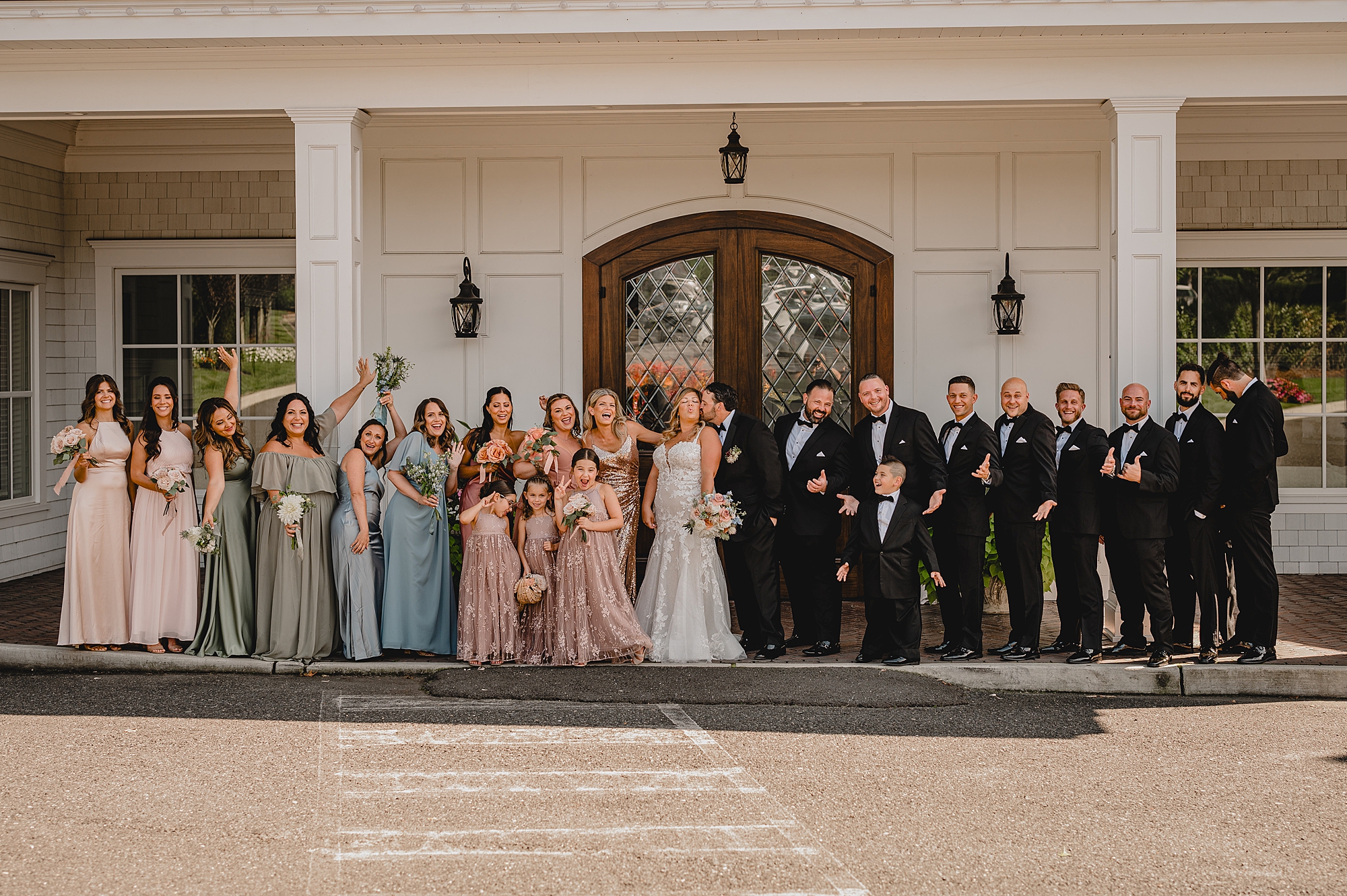 newlyweds stand with wedding party outside the Mill Lakeside Manor