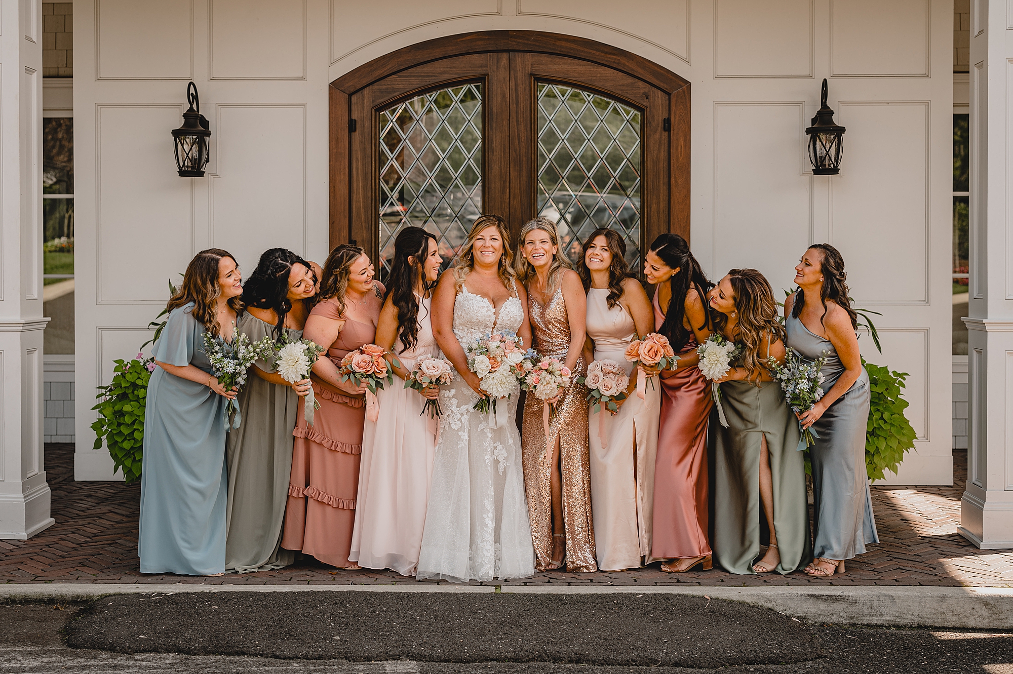 bride poses with bridesmaids in blue, pink, and green gowns