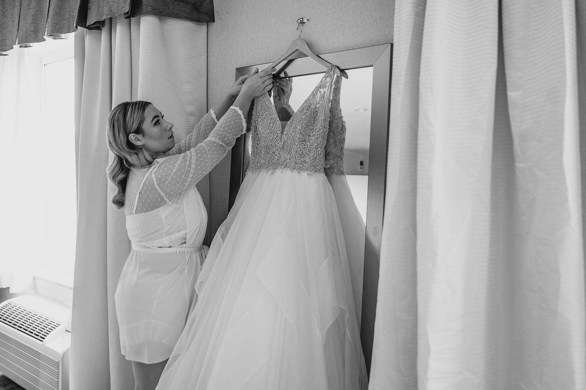 woman hangs bridal gown on mirror in Staten Island hotel