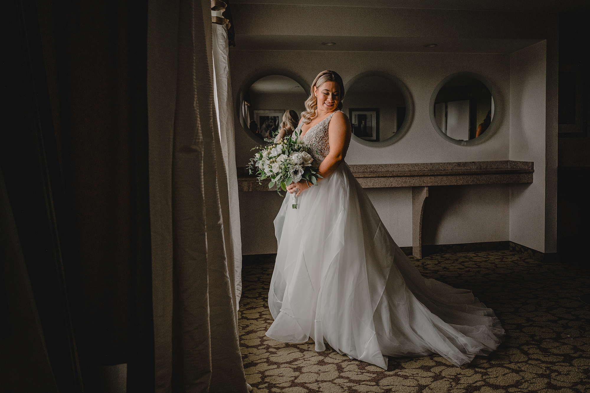 bride looks over shoulder holding bouquet in window of NYC hotel