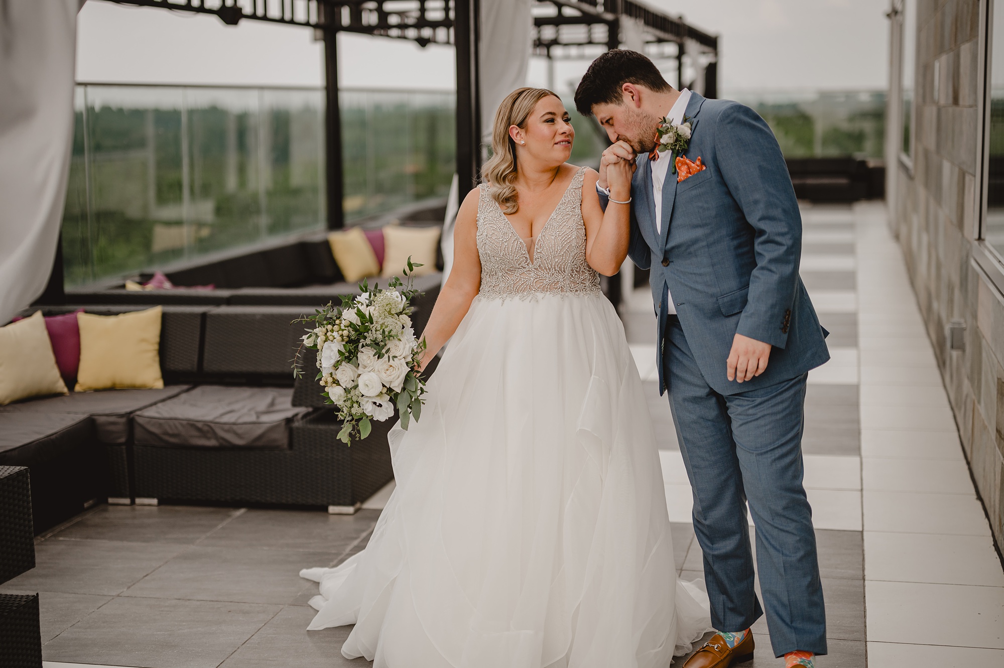 groom leans to kiss bride's hand during first look on patio at Above Staten Island
