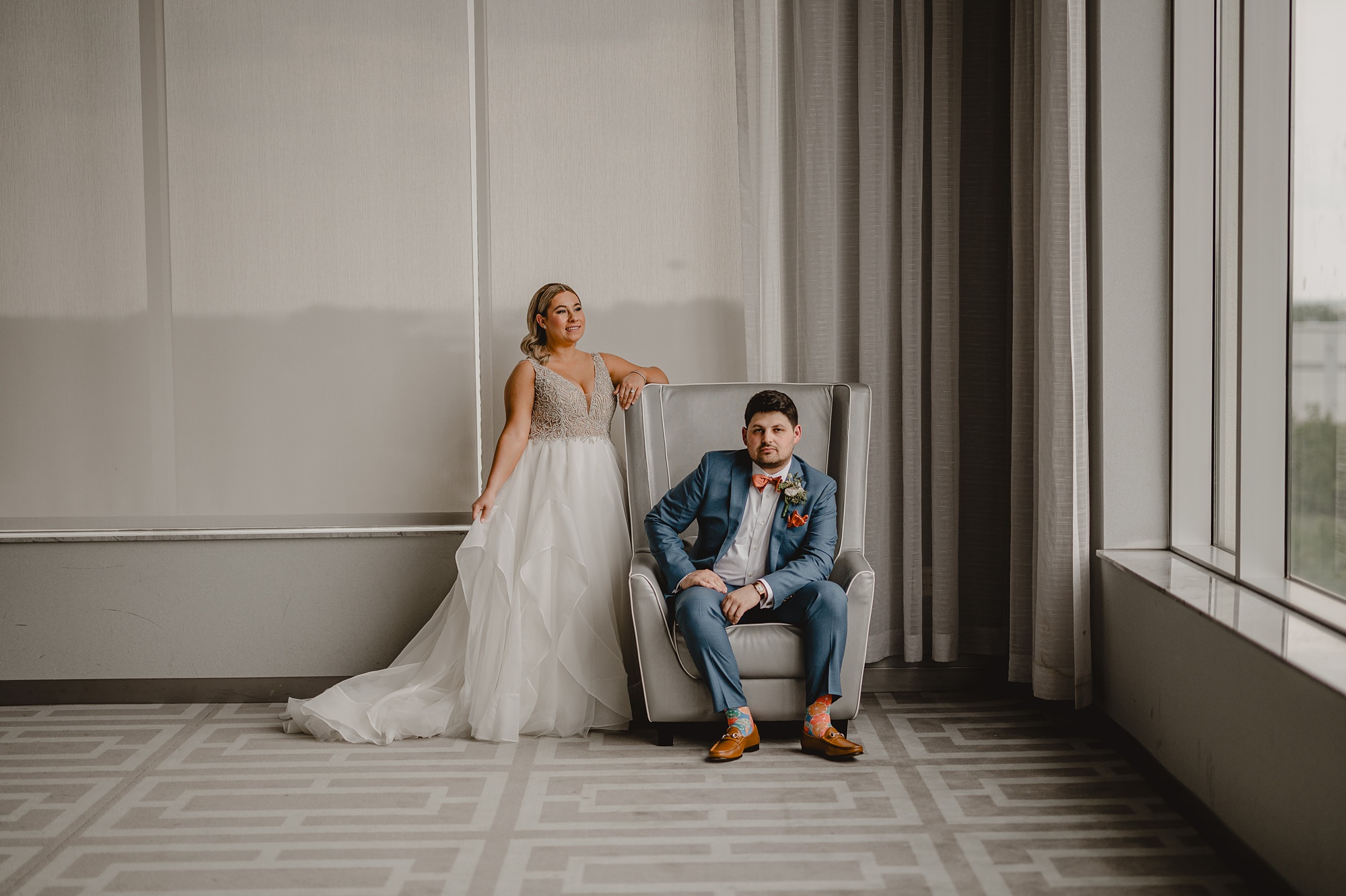 bride leans on back of wingback chair that groom is sitting in