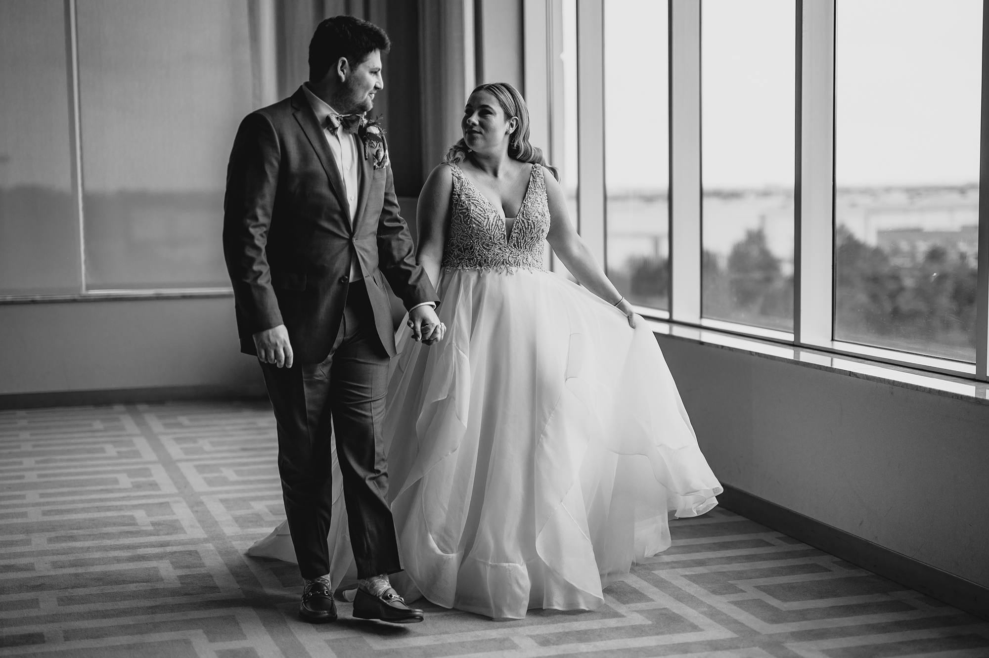 bride and groom hold hands walking across wall of windows at Above Staten Island