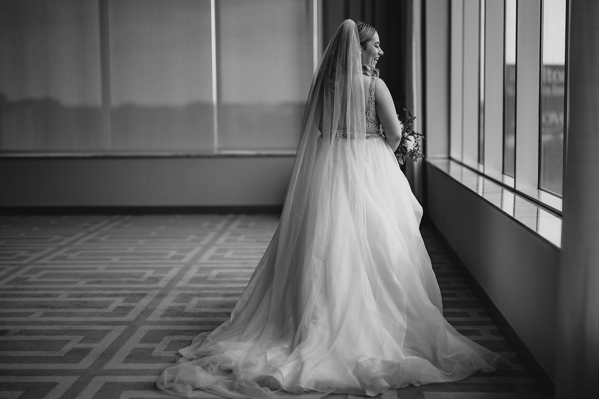 bride looks out window with veil draped around her shoulders at Above Staten Island