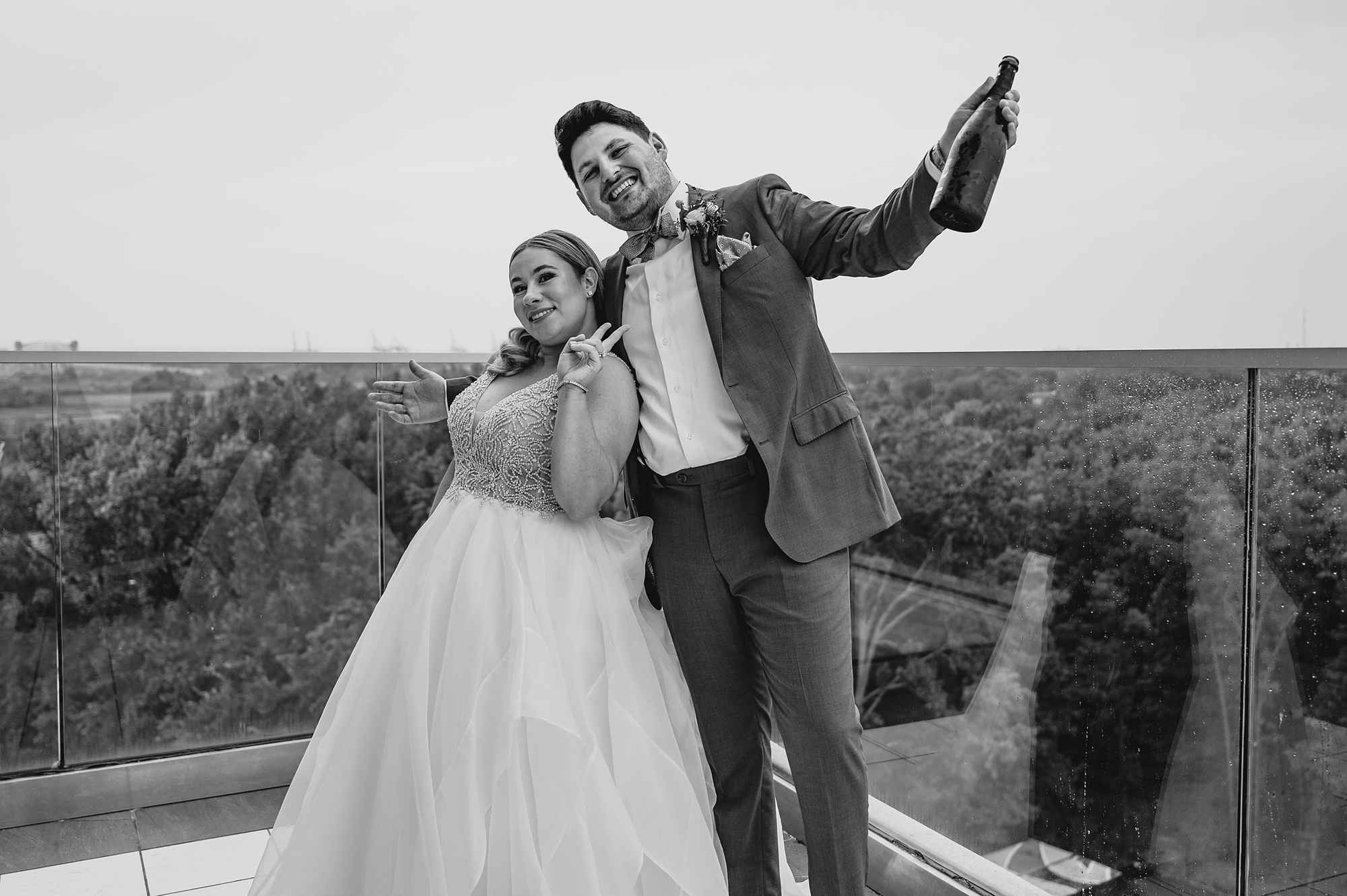 bride and groom hug on rooftop holding bottle of champagne