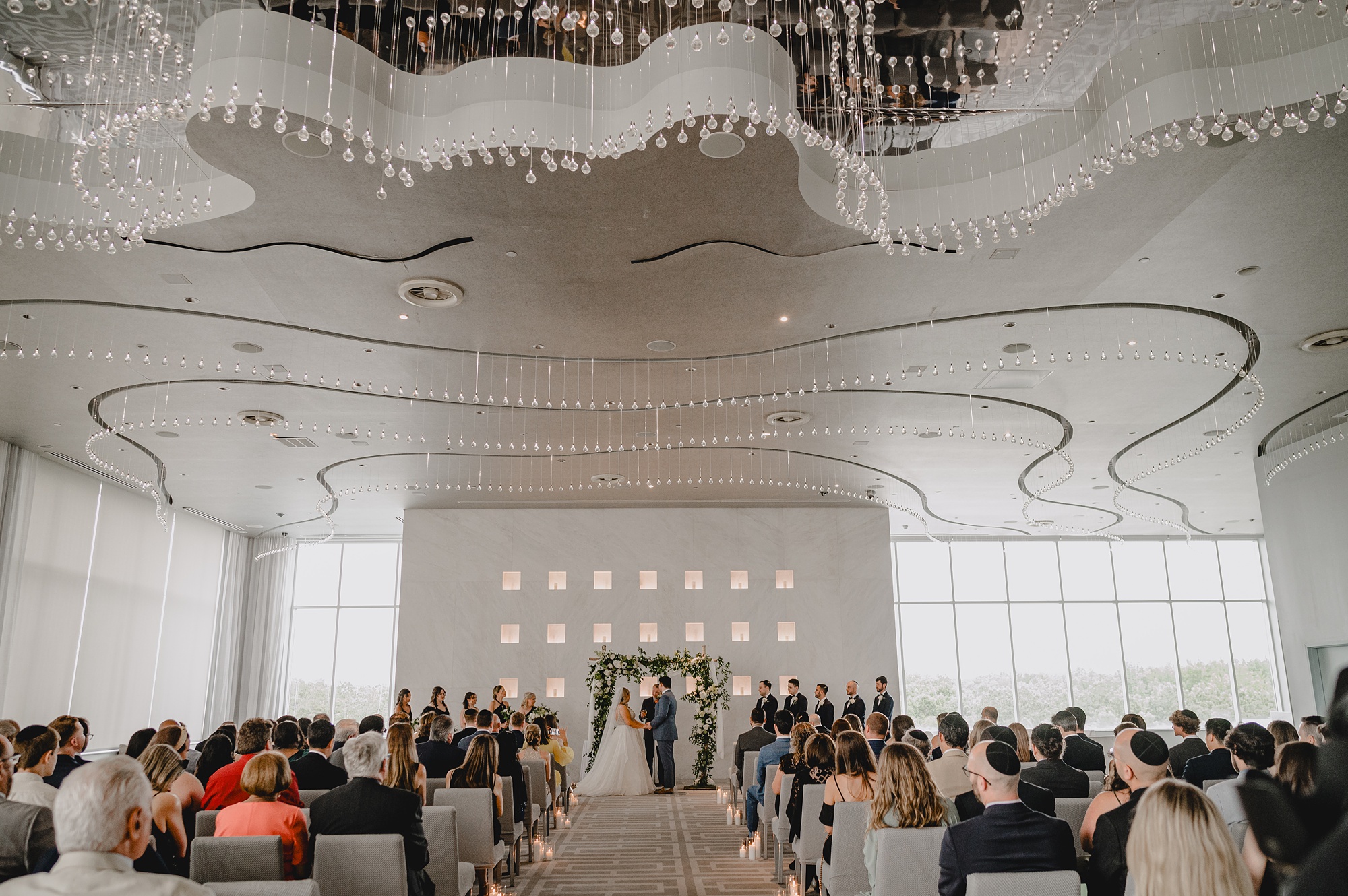 newlyweds hold hands in greenery covered arbor during wedding ceremony at Above Staten Island