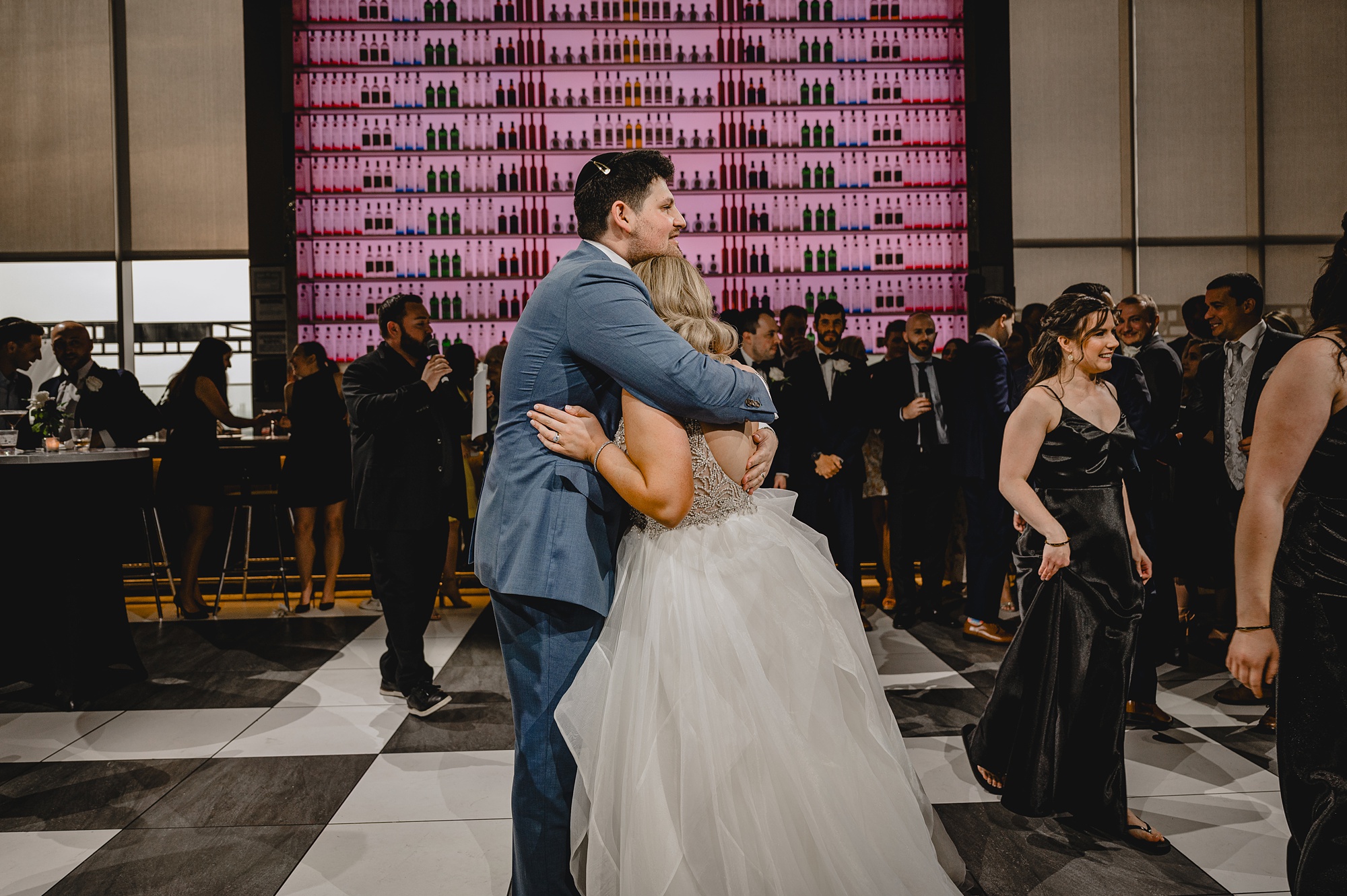 bride and groom hug on dance floor in front of pink bar at Above Staten Island