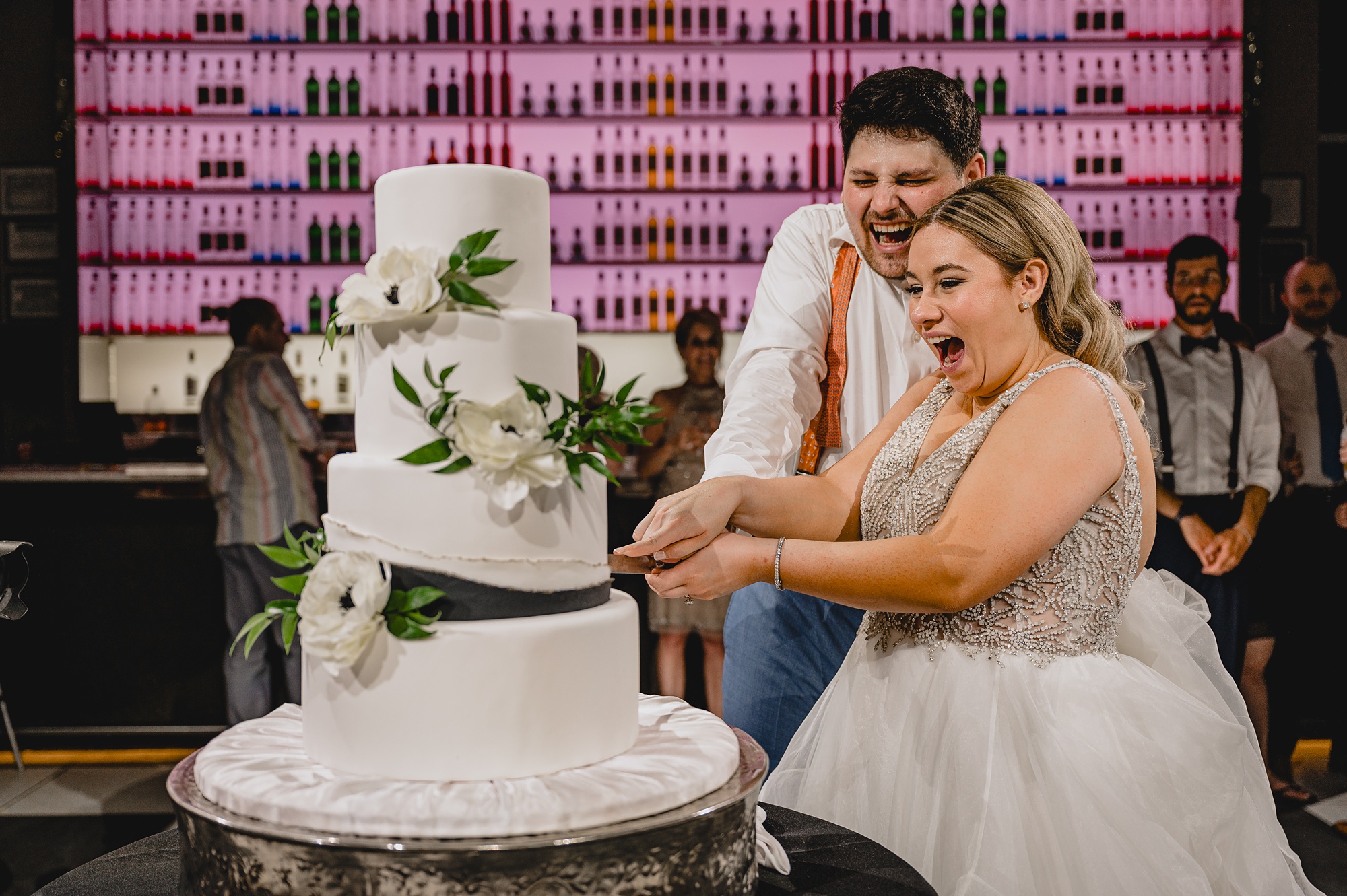 newlyweds laugh cutting tiered wedding cake