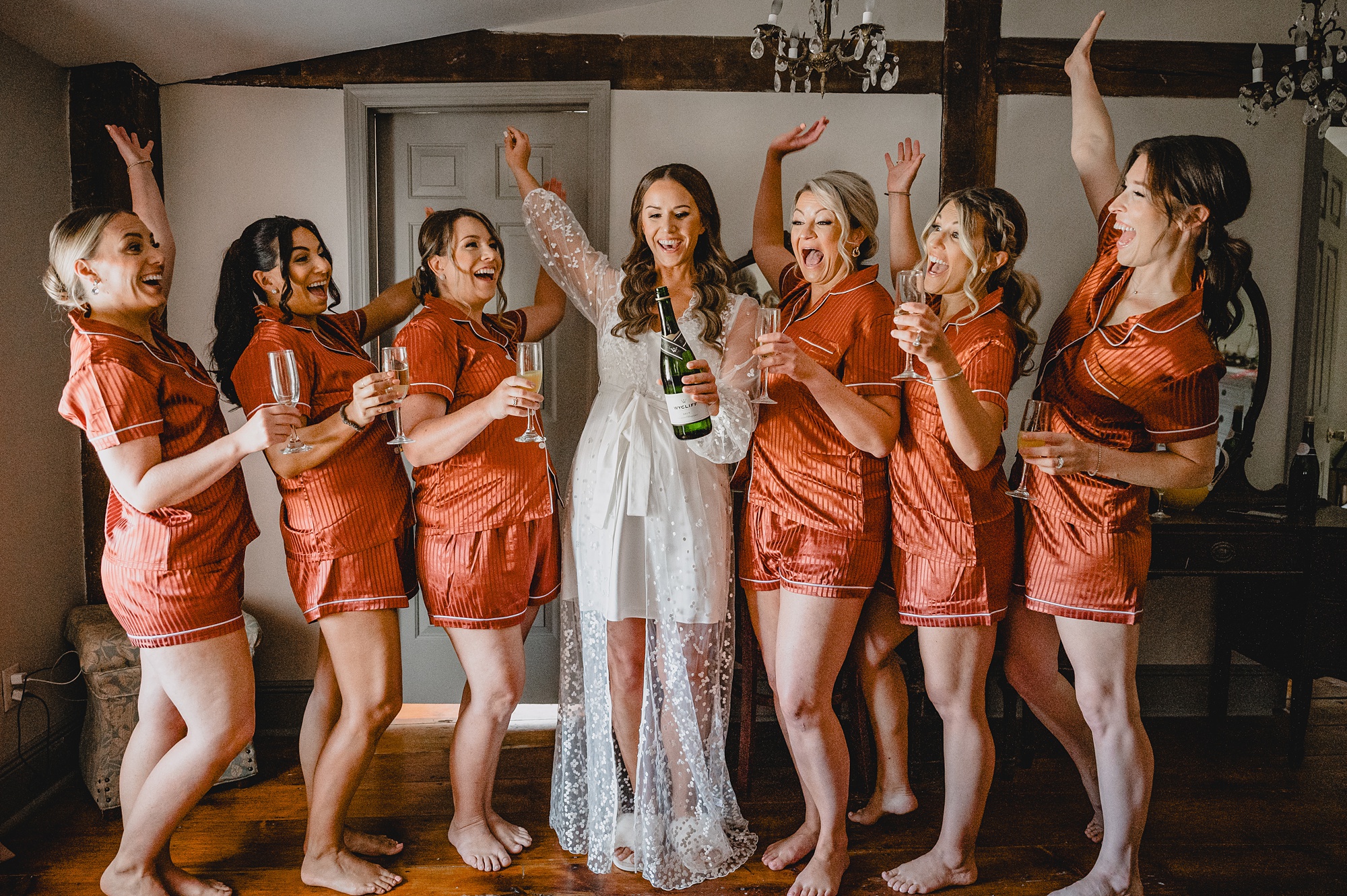 bride and bridesmaids in orange robes cheer during prep at David's Country Inn