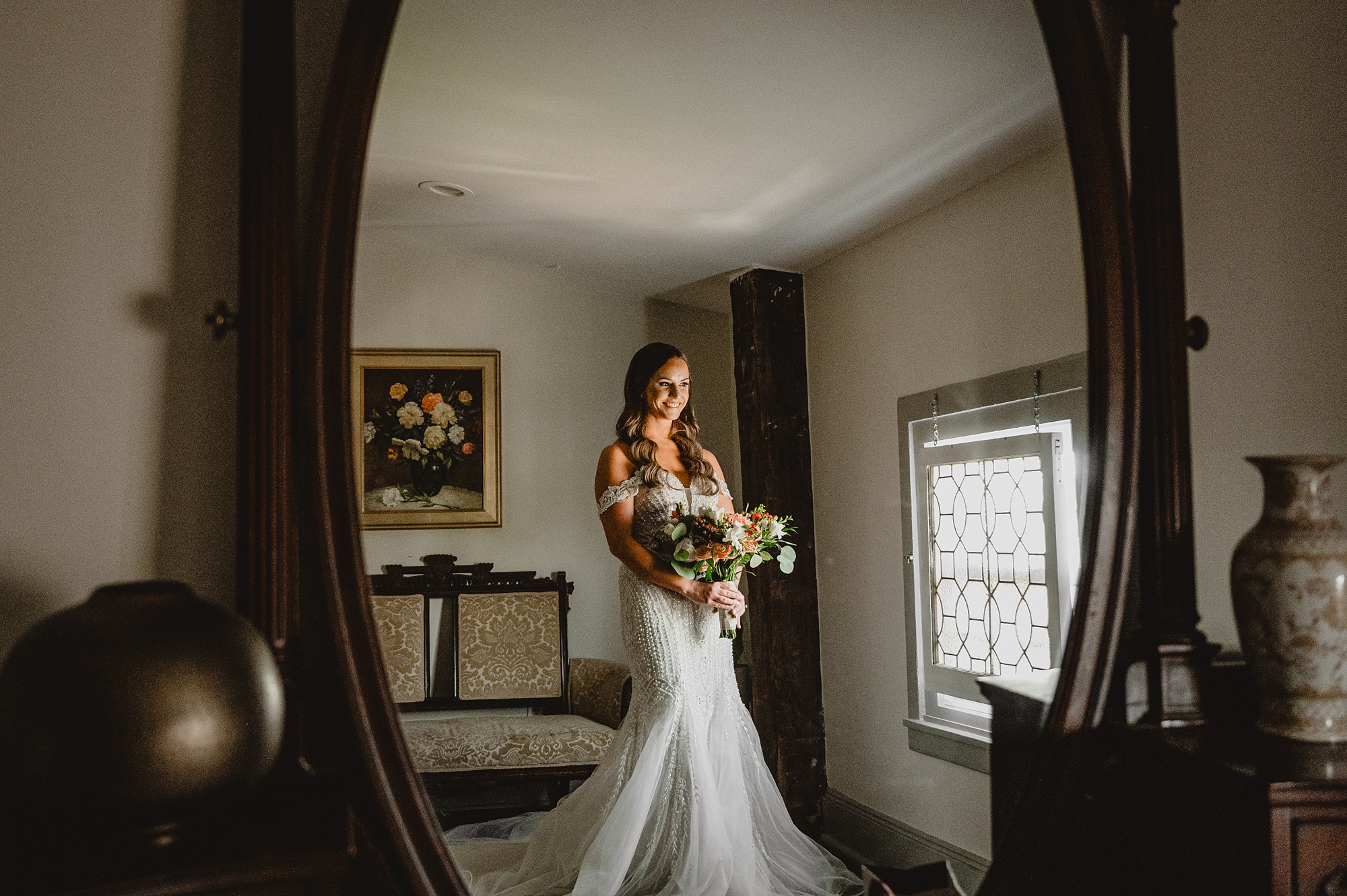 bride holds bouquet of flowers in wedding gown in mirror reflection at David's Country Inn