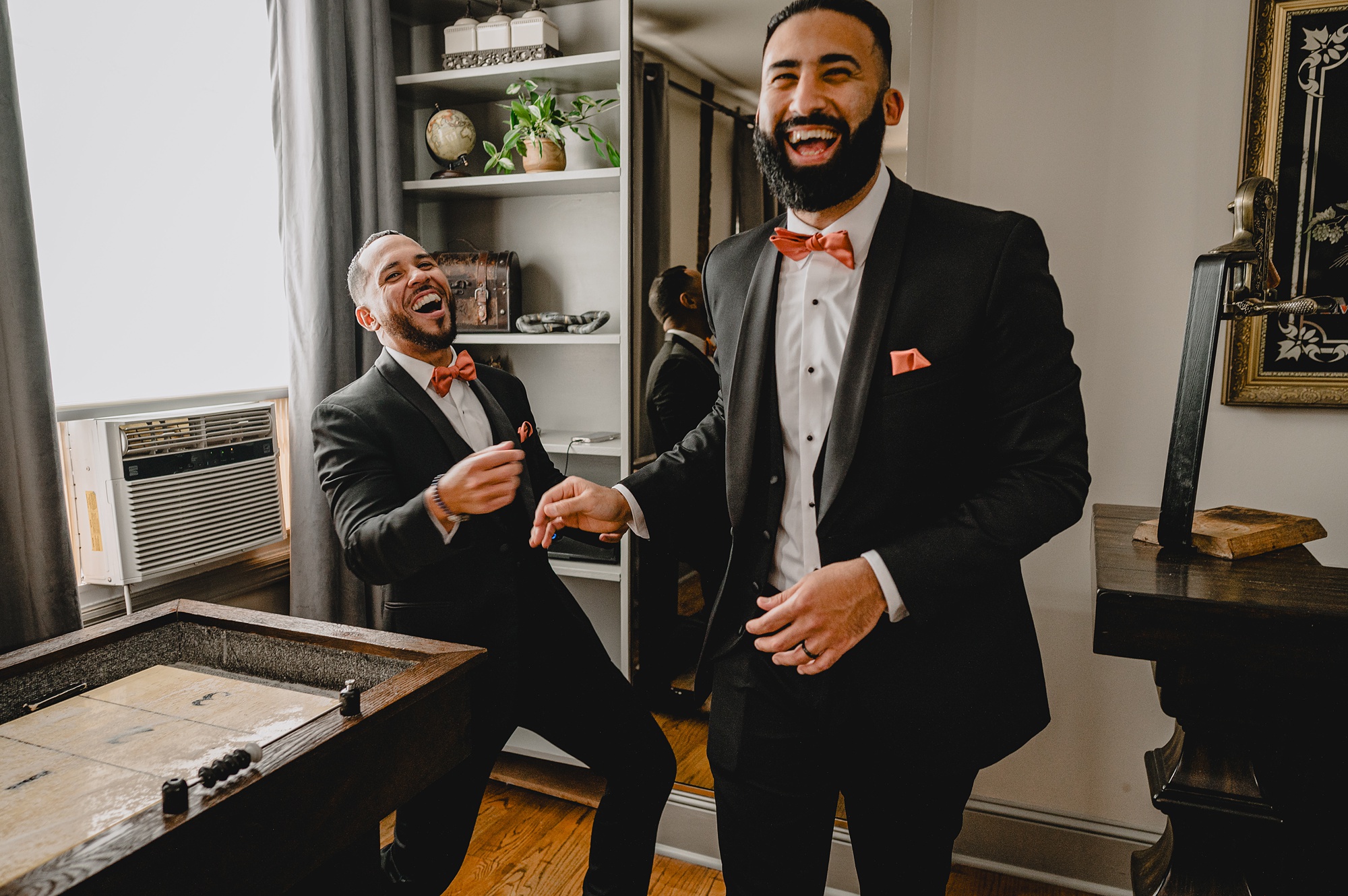 groom and groomsmen in black suits laugh together in front of board