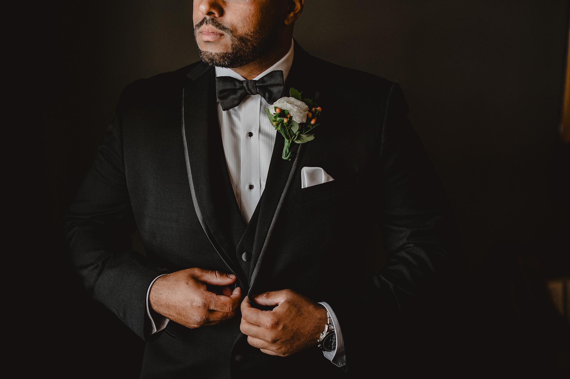 groom holds lapel of suit buttoning up buttons