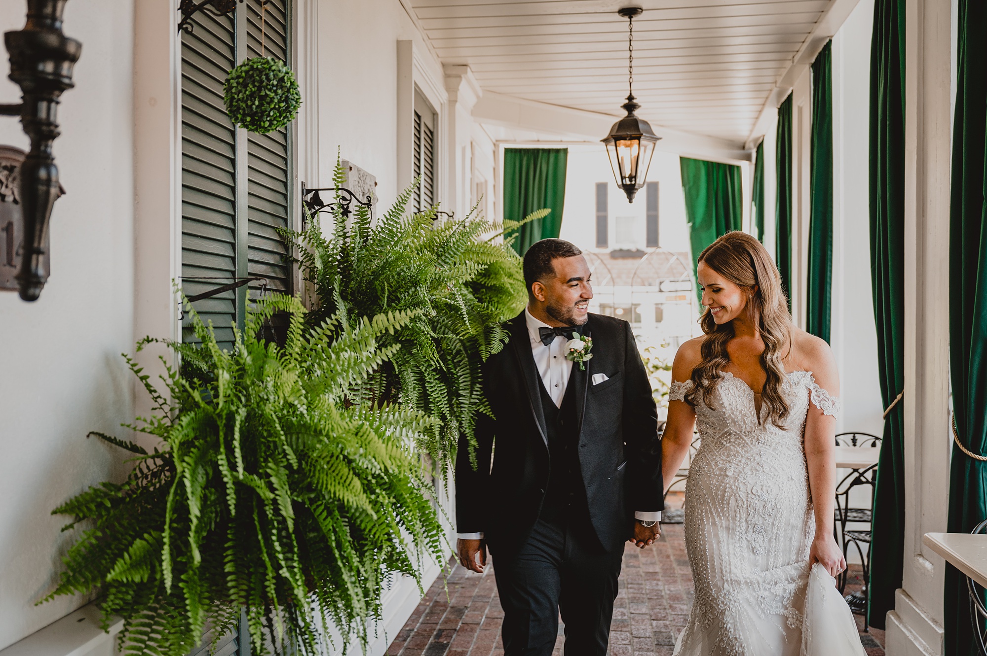 bride and groom hold hands walking under patio