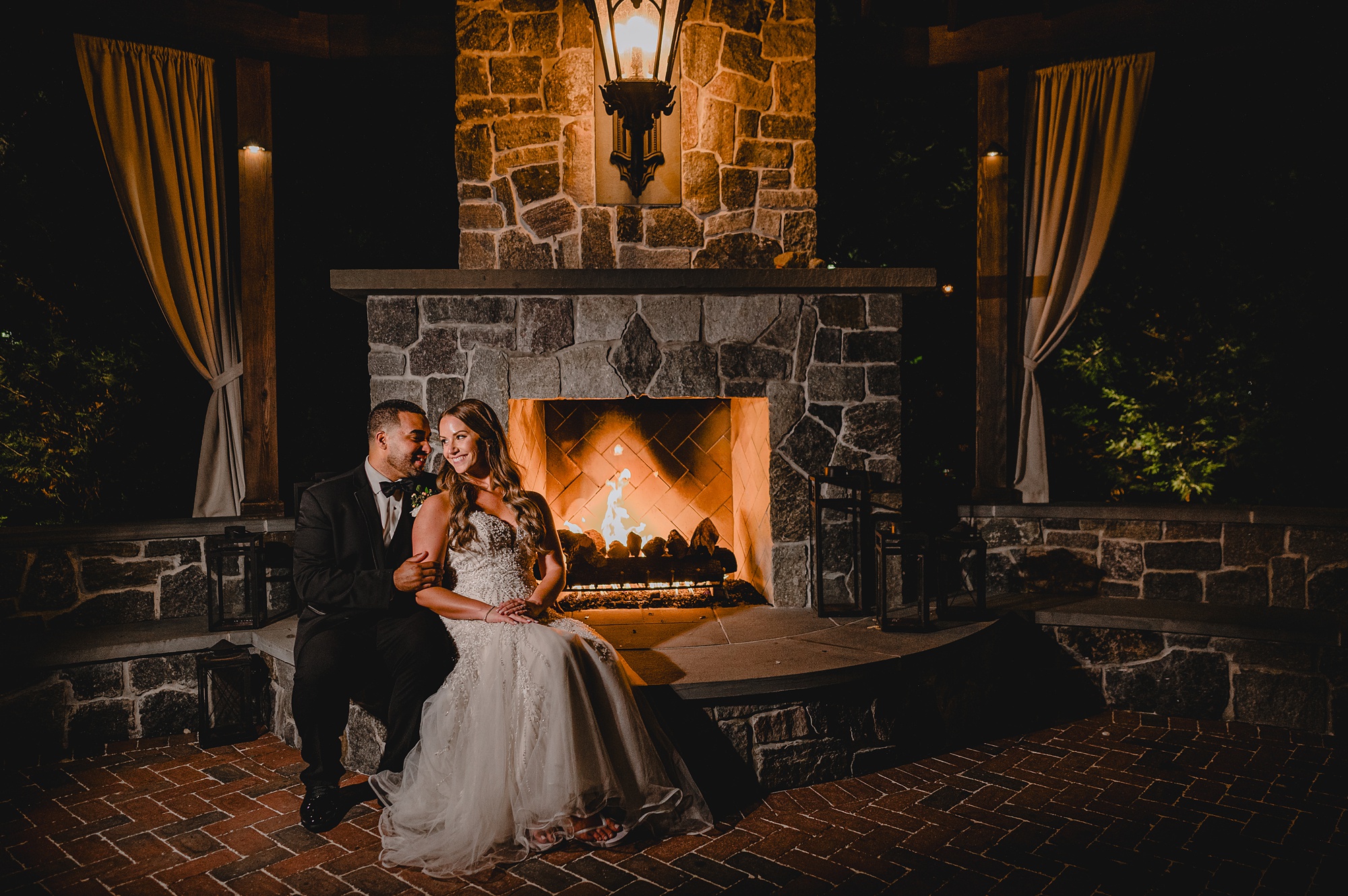 newlyweds snuggle on patio in front of stone fireplace in Hackettstown NJ