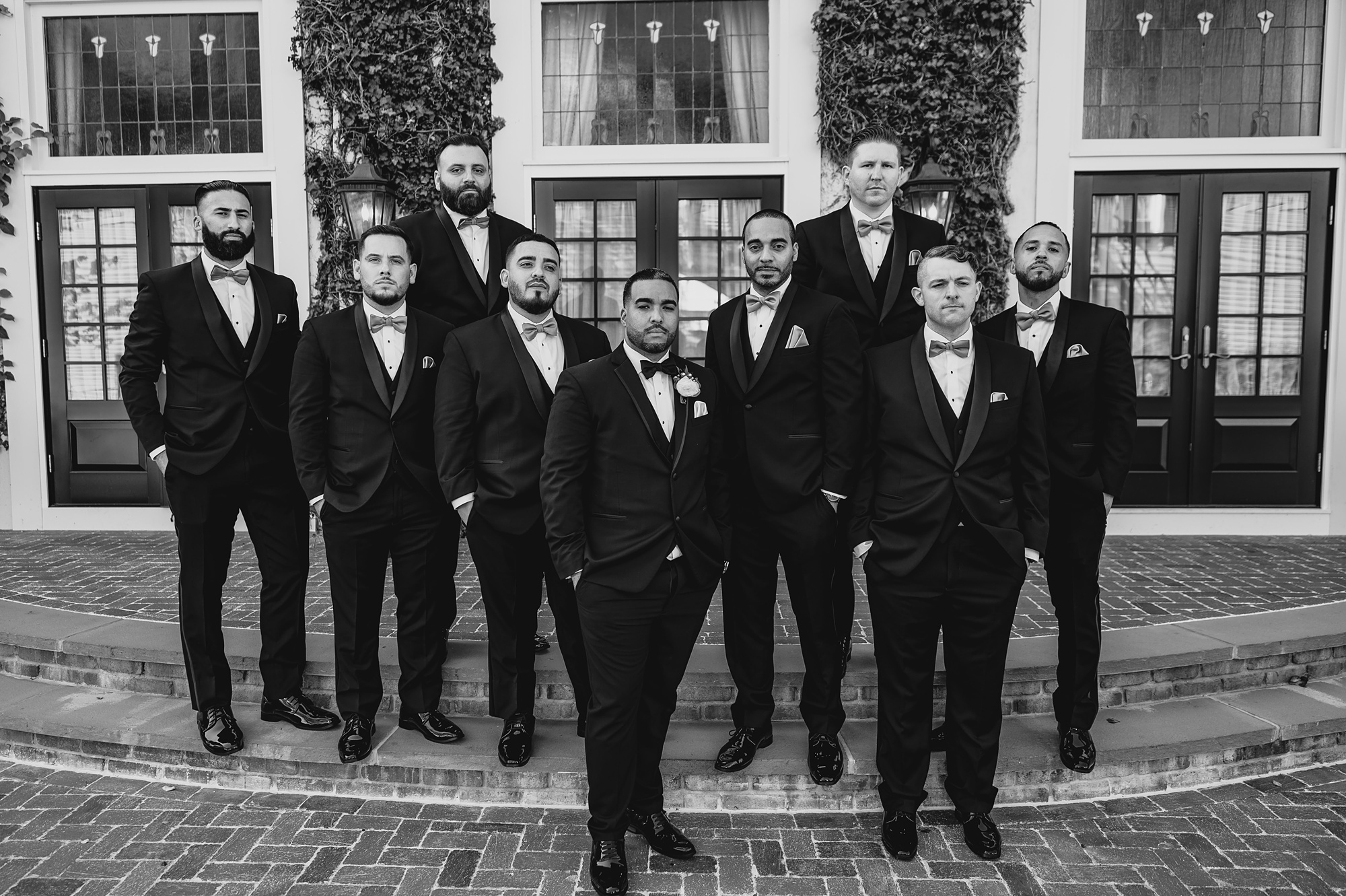 groom stands with groomsmen on brick steps of patio at David's Country Inn