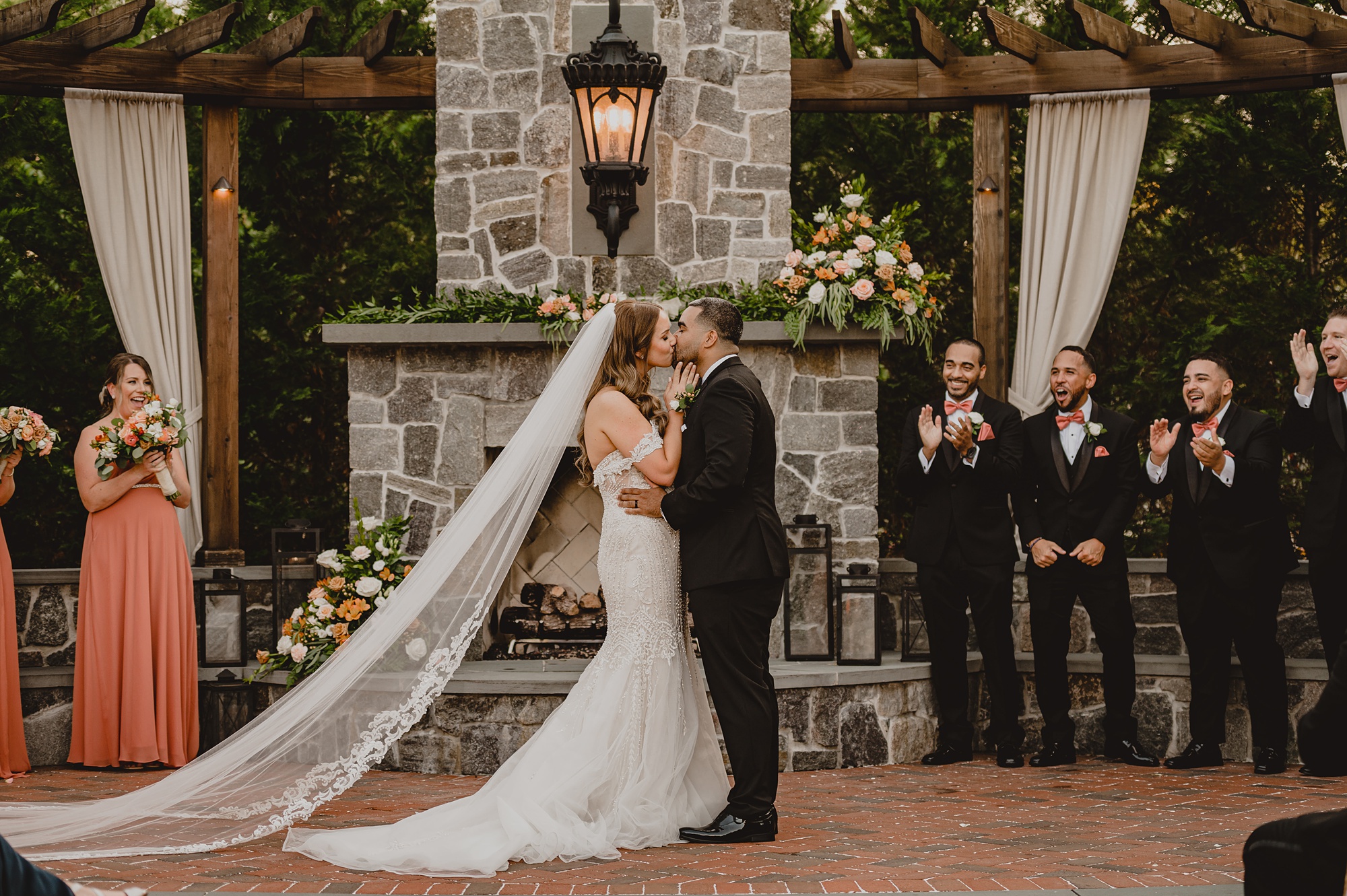 bride and groom kiss in front of stone fireplace during wedding ceremony on brick patio at David's Country Inn