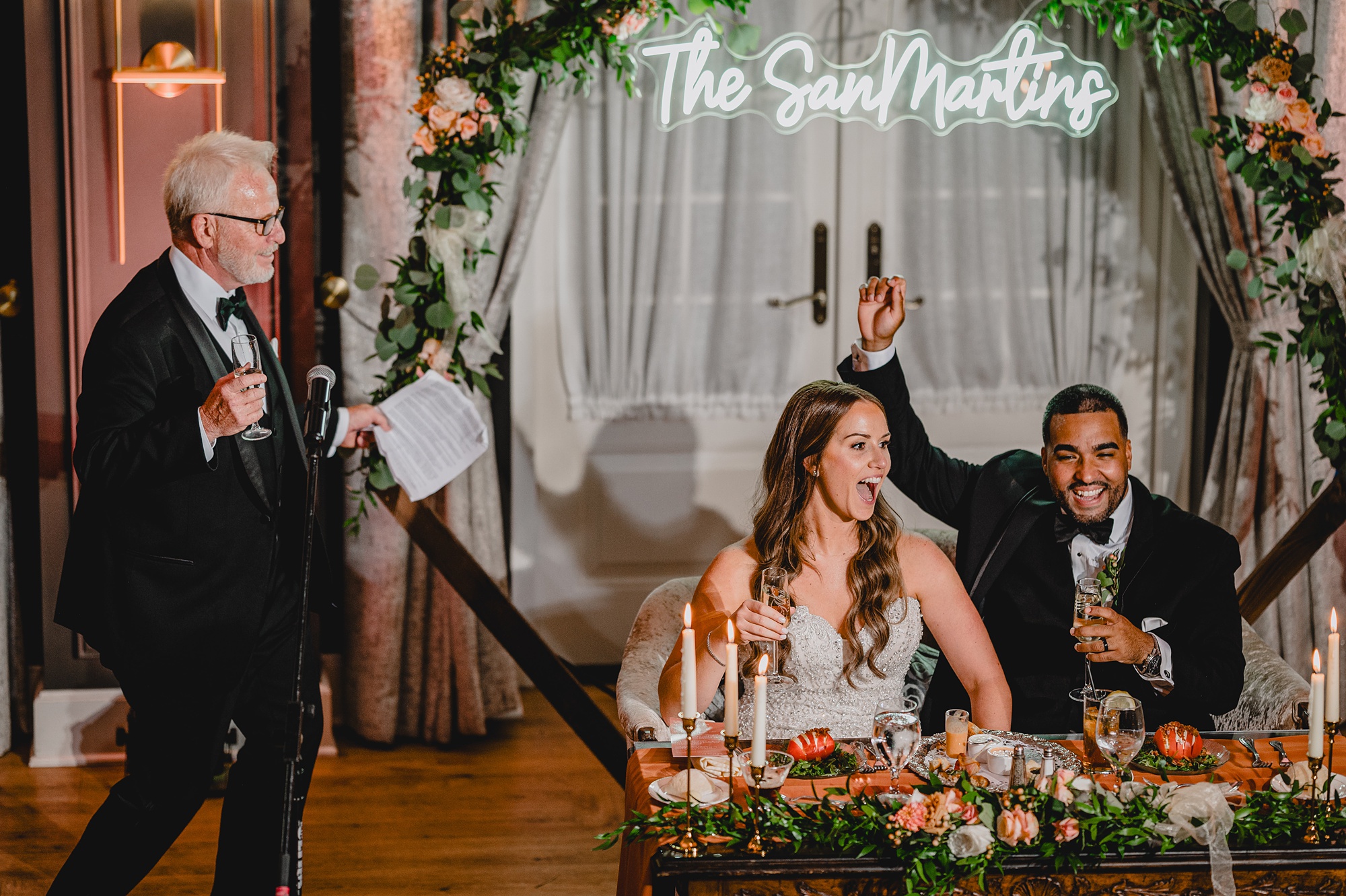 bride and groom cheer during wedding reception sitting at sweetheart table