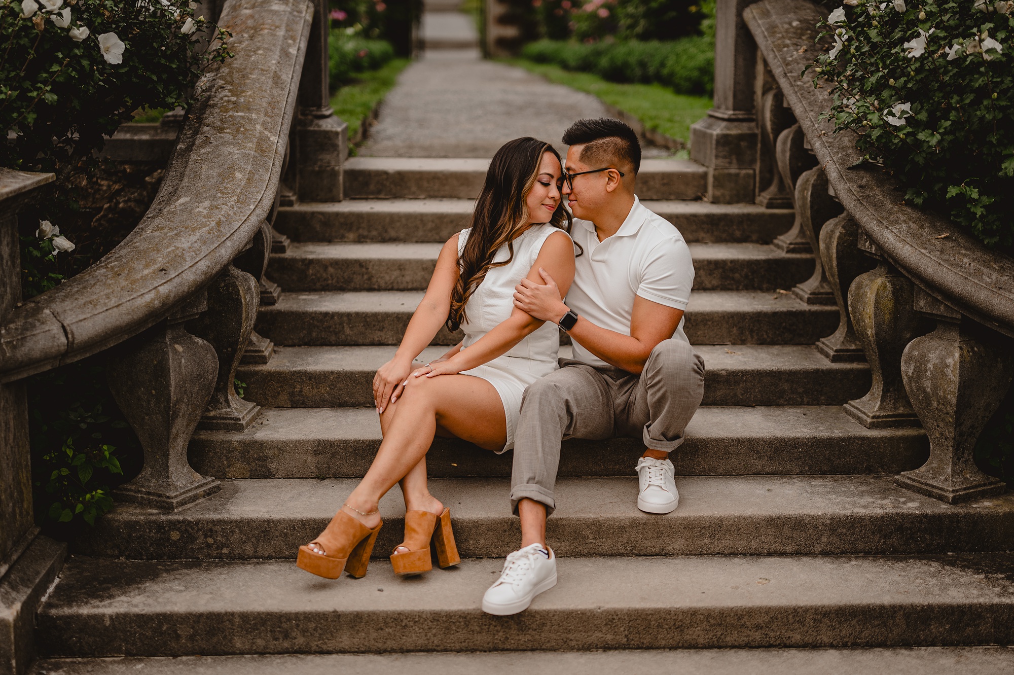 engaged couple cuddles on stone steps at Old Westbury Gardens