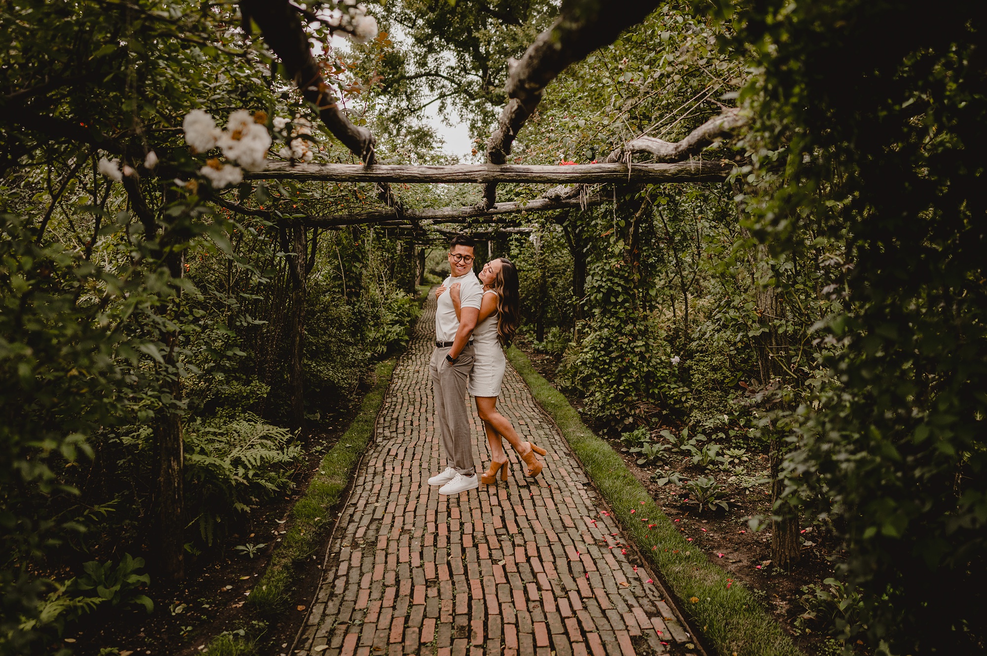 man and woman hug under arbor over walkway in gardens 