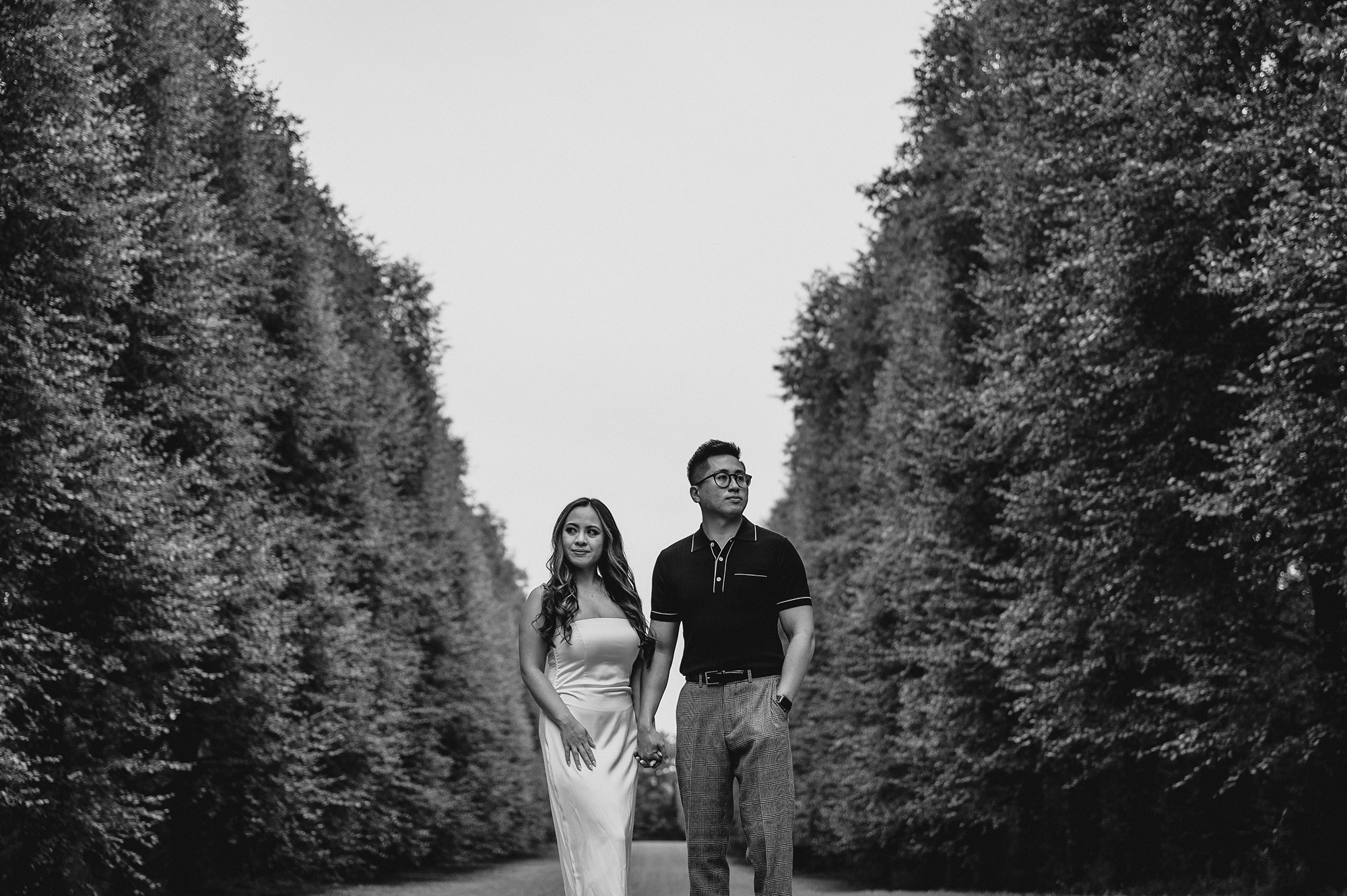 man and woman hold hands between rows of trees at Old Westbury Gardens