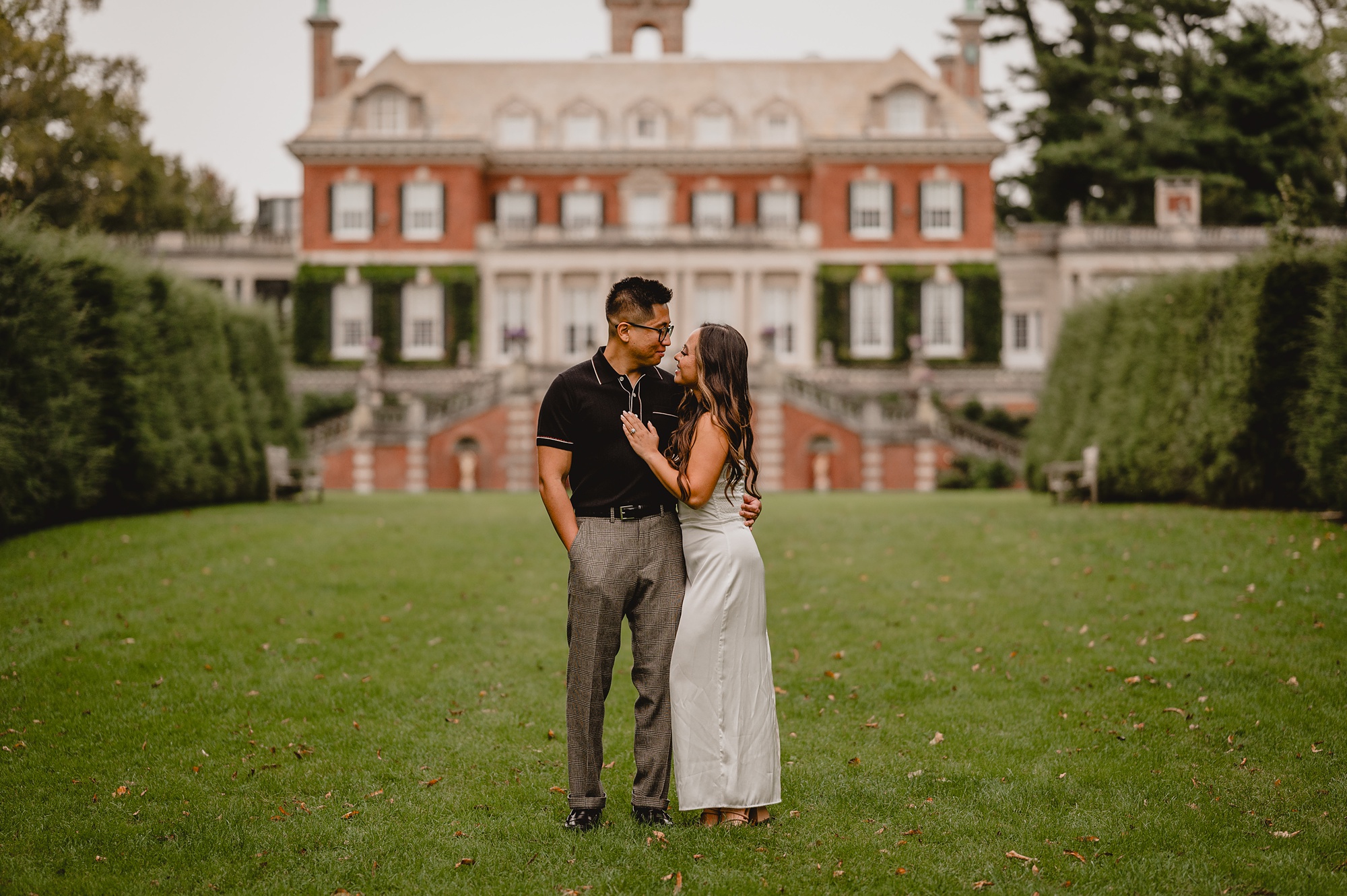 man and woman hug in front of mansion on grounds of Old Westbury Gardens