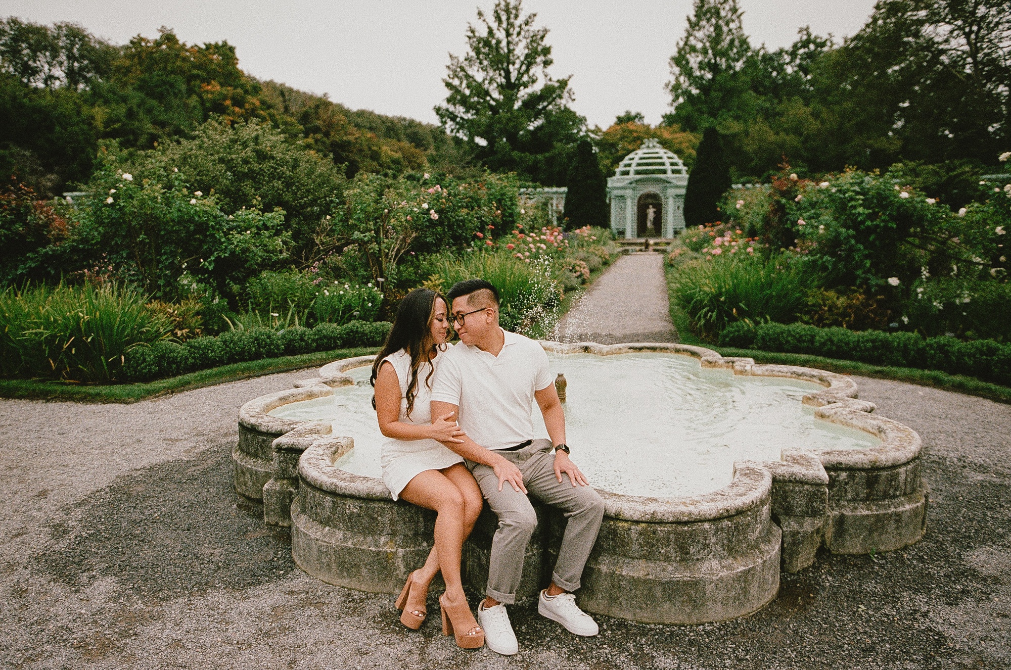 engaged couple sits on fountain inside gardens at Old Westbury Gardens