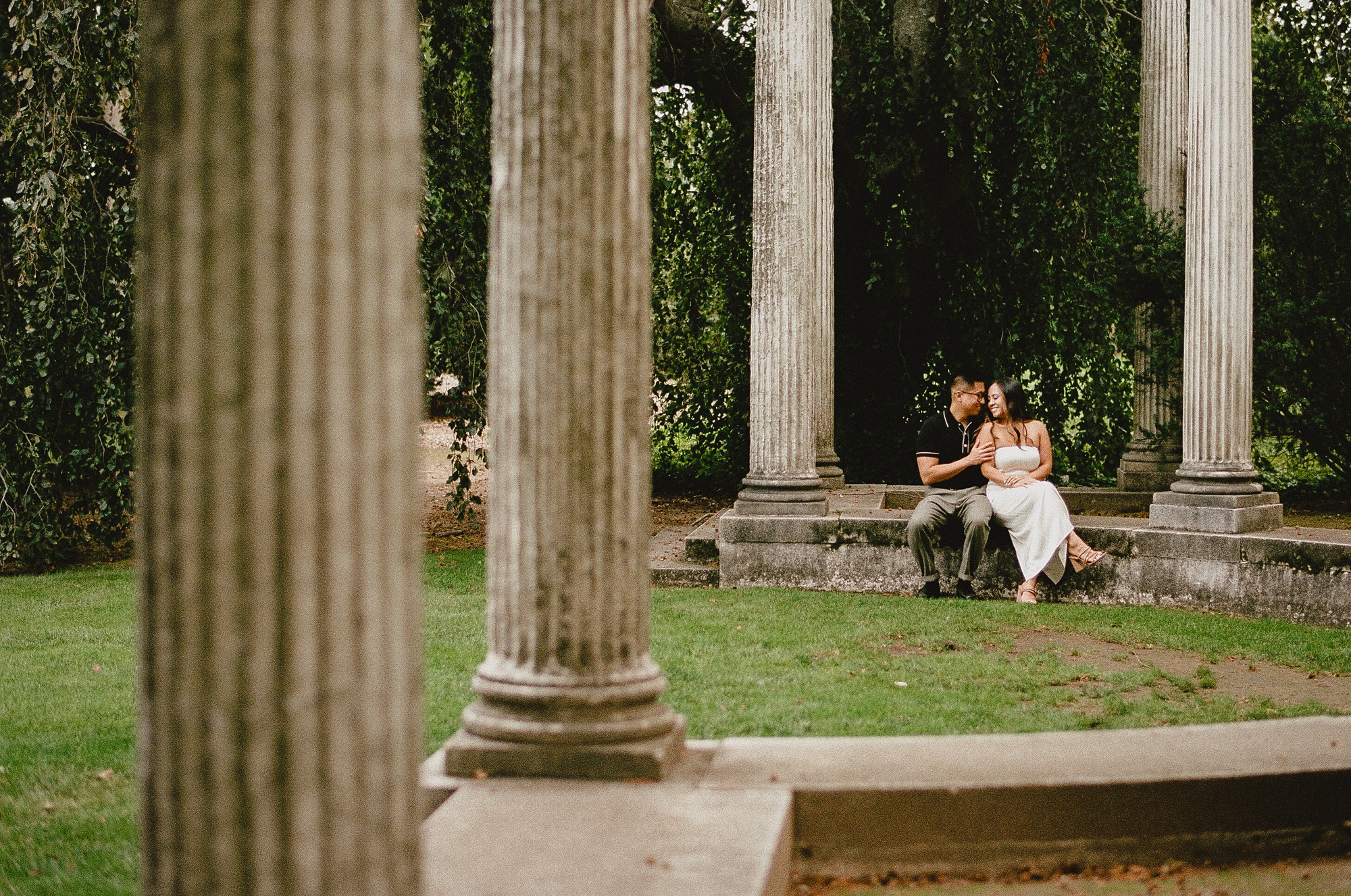 couple sits between pillars in gardens 