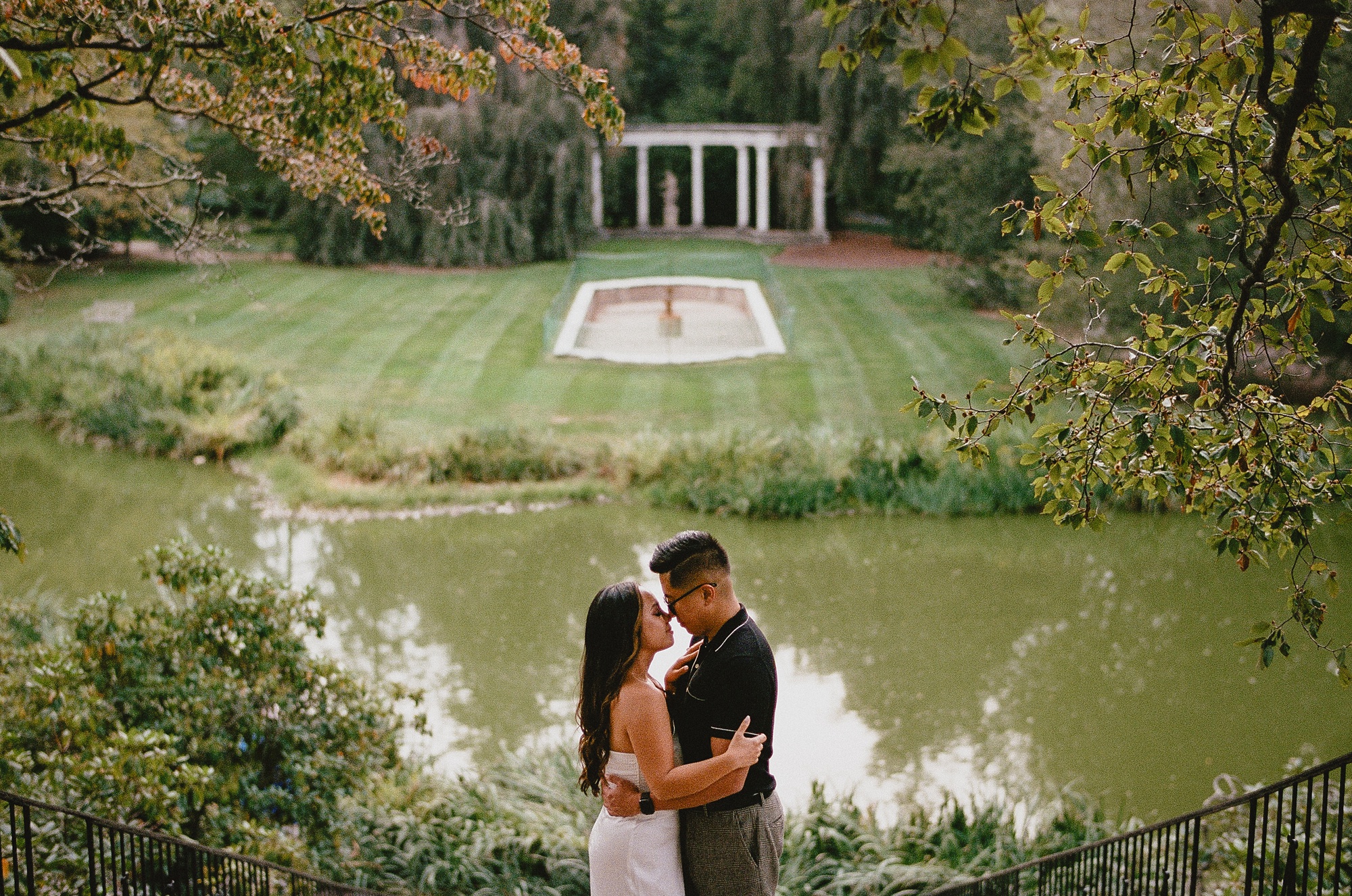 engaged couple hugs with pond behind them at Old Westbury Gardens