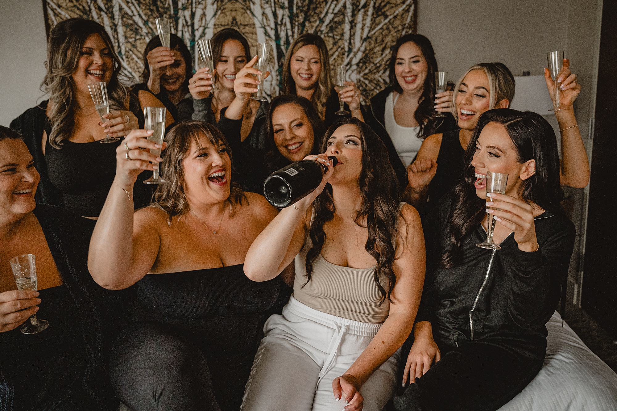 bride and bridesmaids drink champagne toasting in hotel room