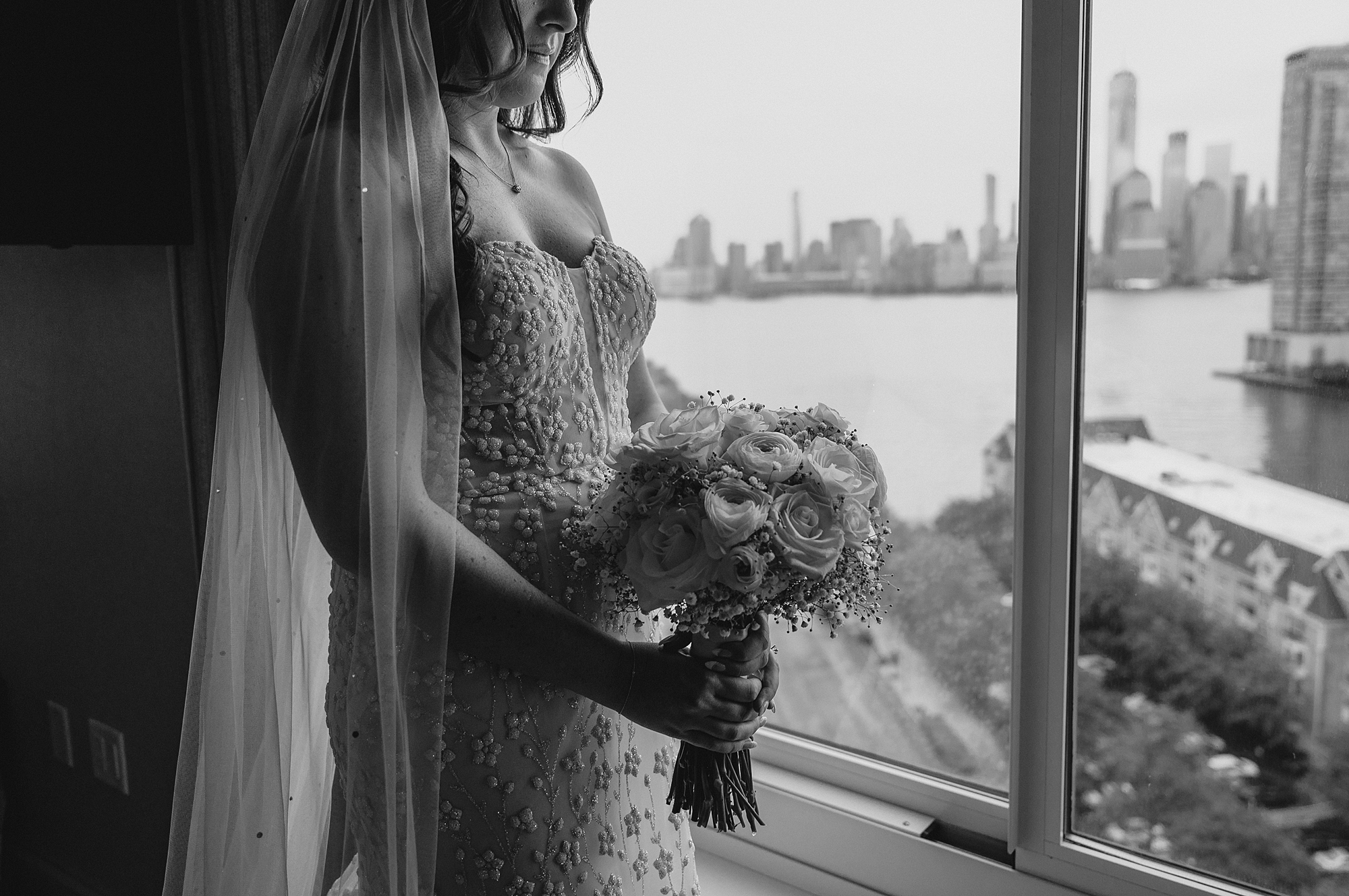 bride holds bouquet of roses looking out window of Jersey City hotel