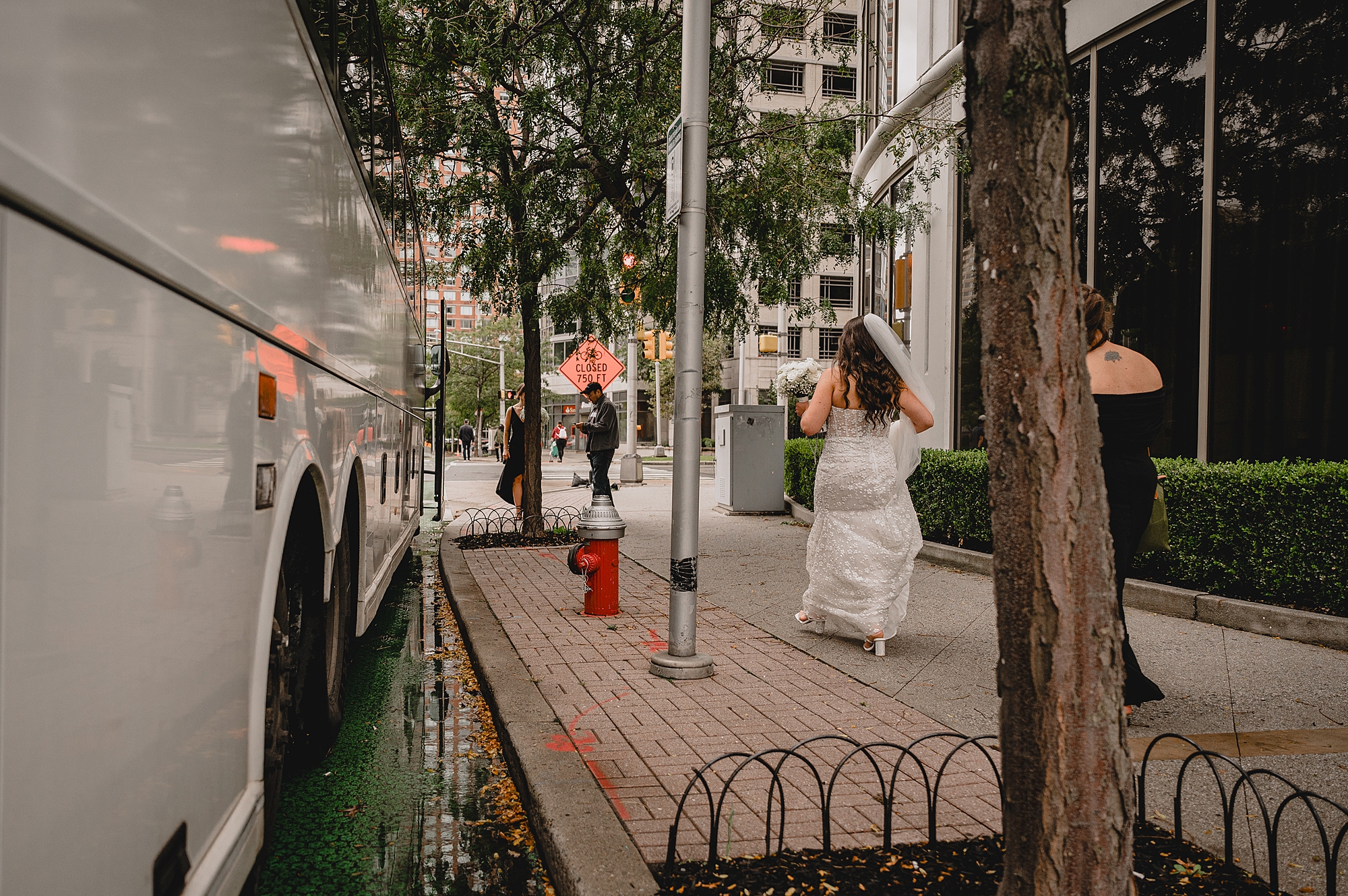 bride walks down sidewalk in Jersey City holding skirt of wedding gown