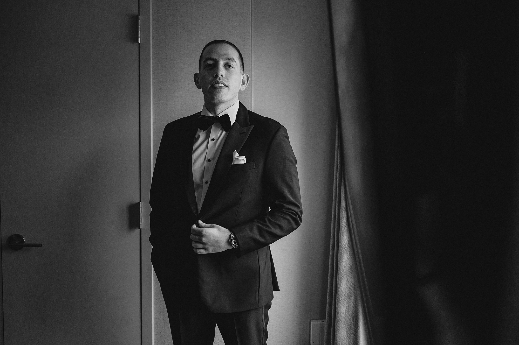 groom stands with hand on buttons of tux jacket