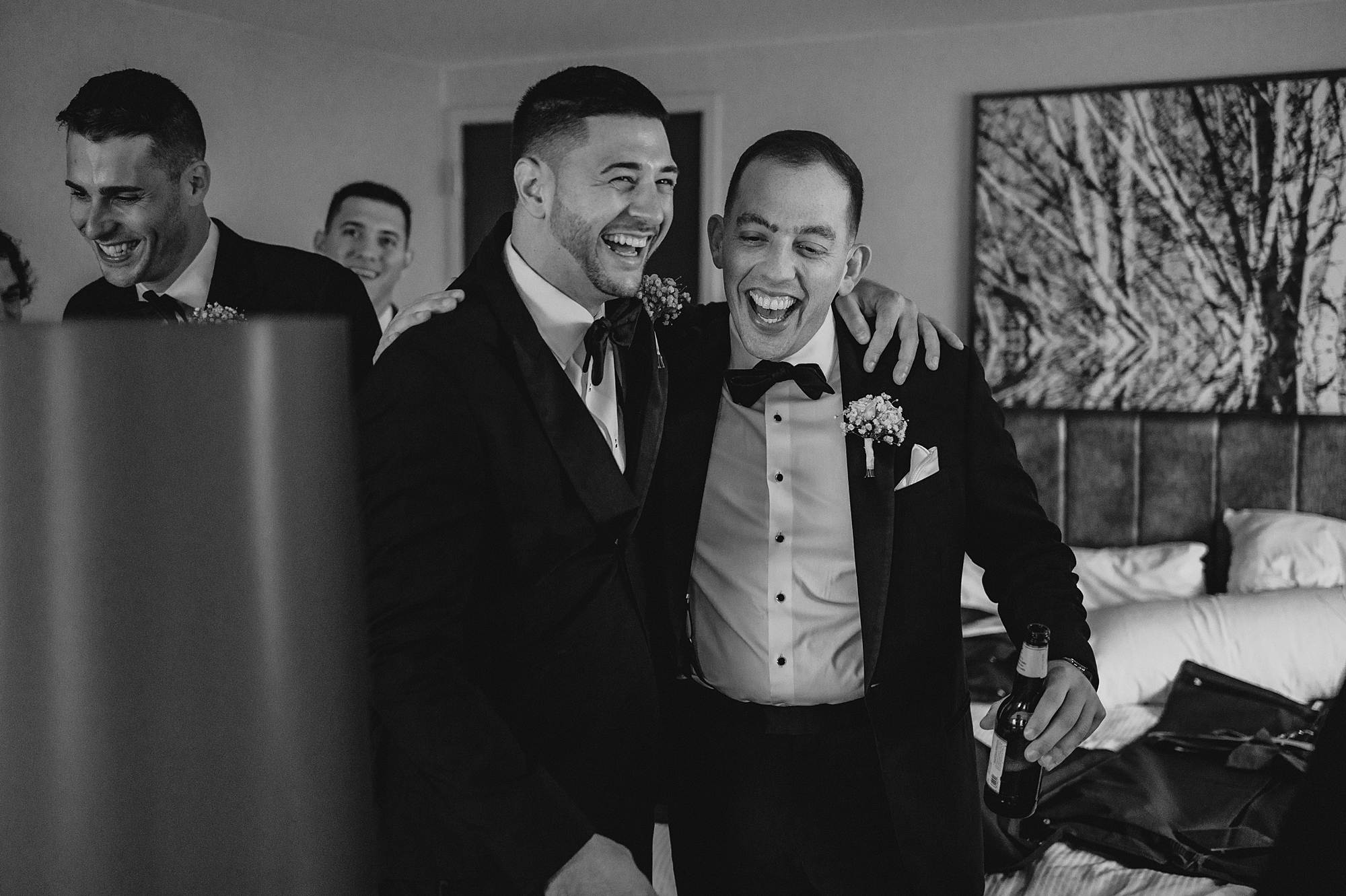 groomsman hugs groom around shoulders in hotel room in Jersey City