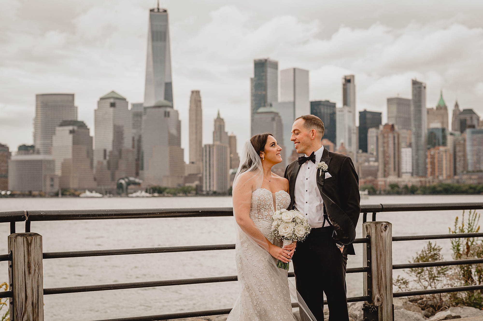 bride and groom smile get each other against railing of the Hudson River