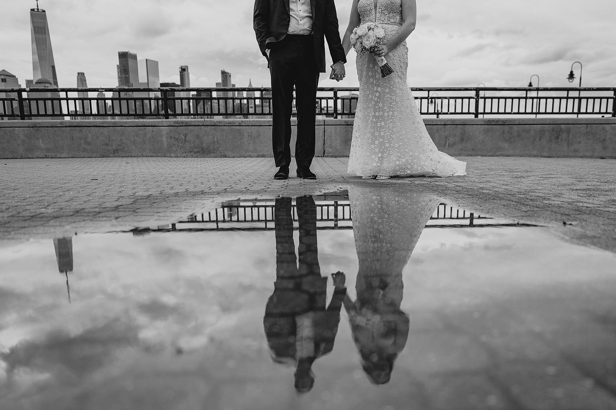 bride and groom hold hands reflected in puddle of water