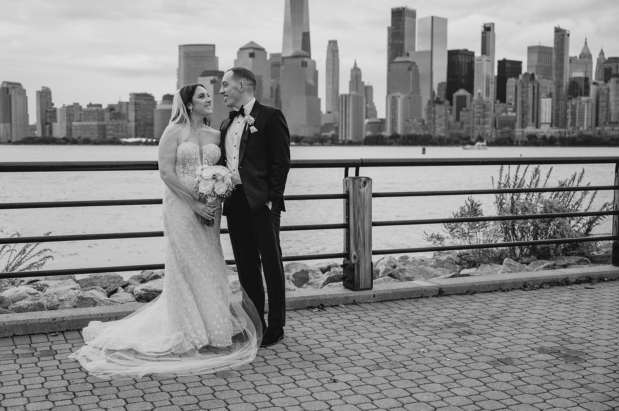 groom smiles at bride in front of railing overlooking Hudson River