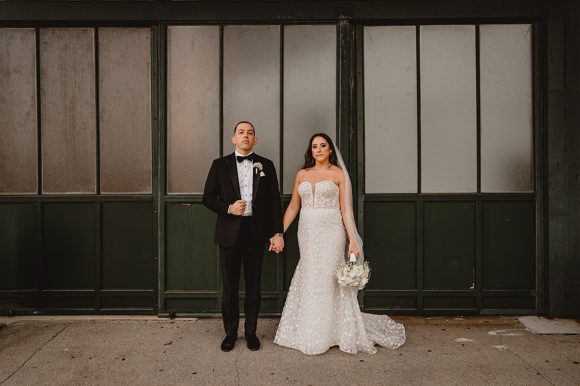 bride and groom stand holding hands in front of black and white inwdows