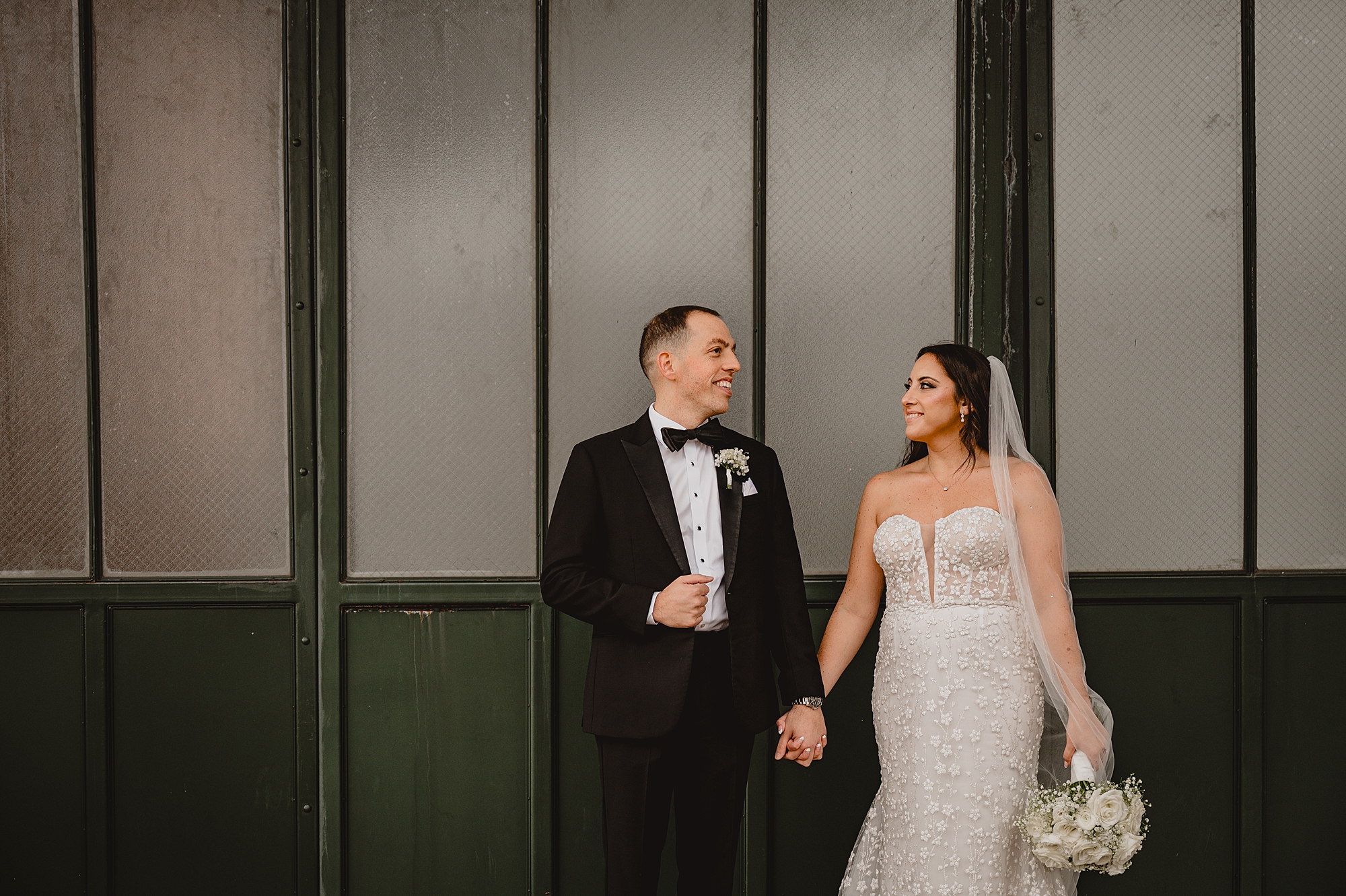 bride and groom hold hands by green windows