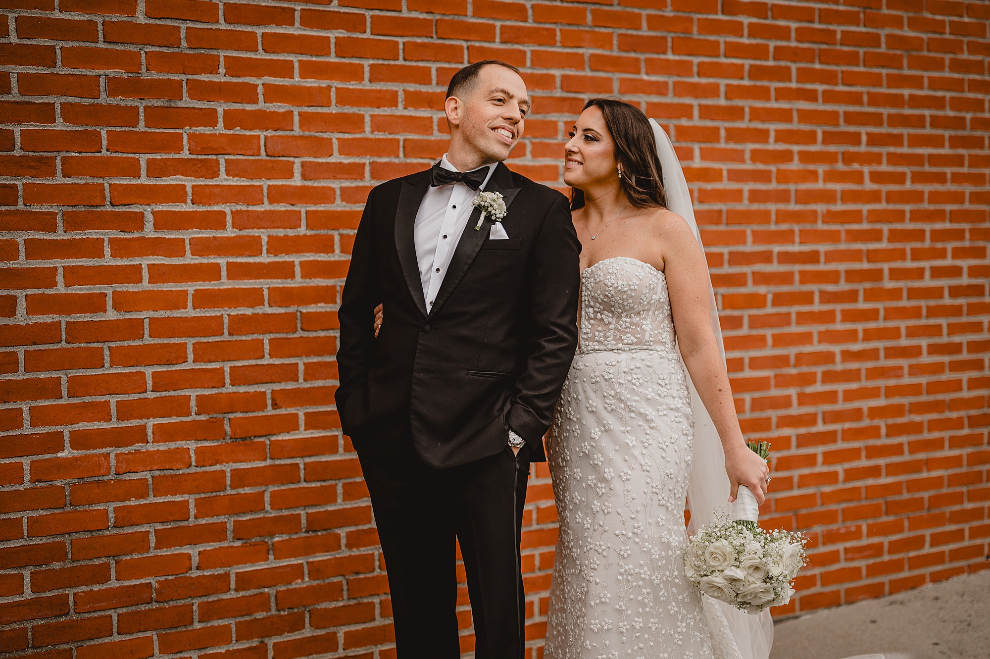 bride smiles over groom's shoulder leaning to kiss his shoulder