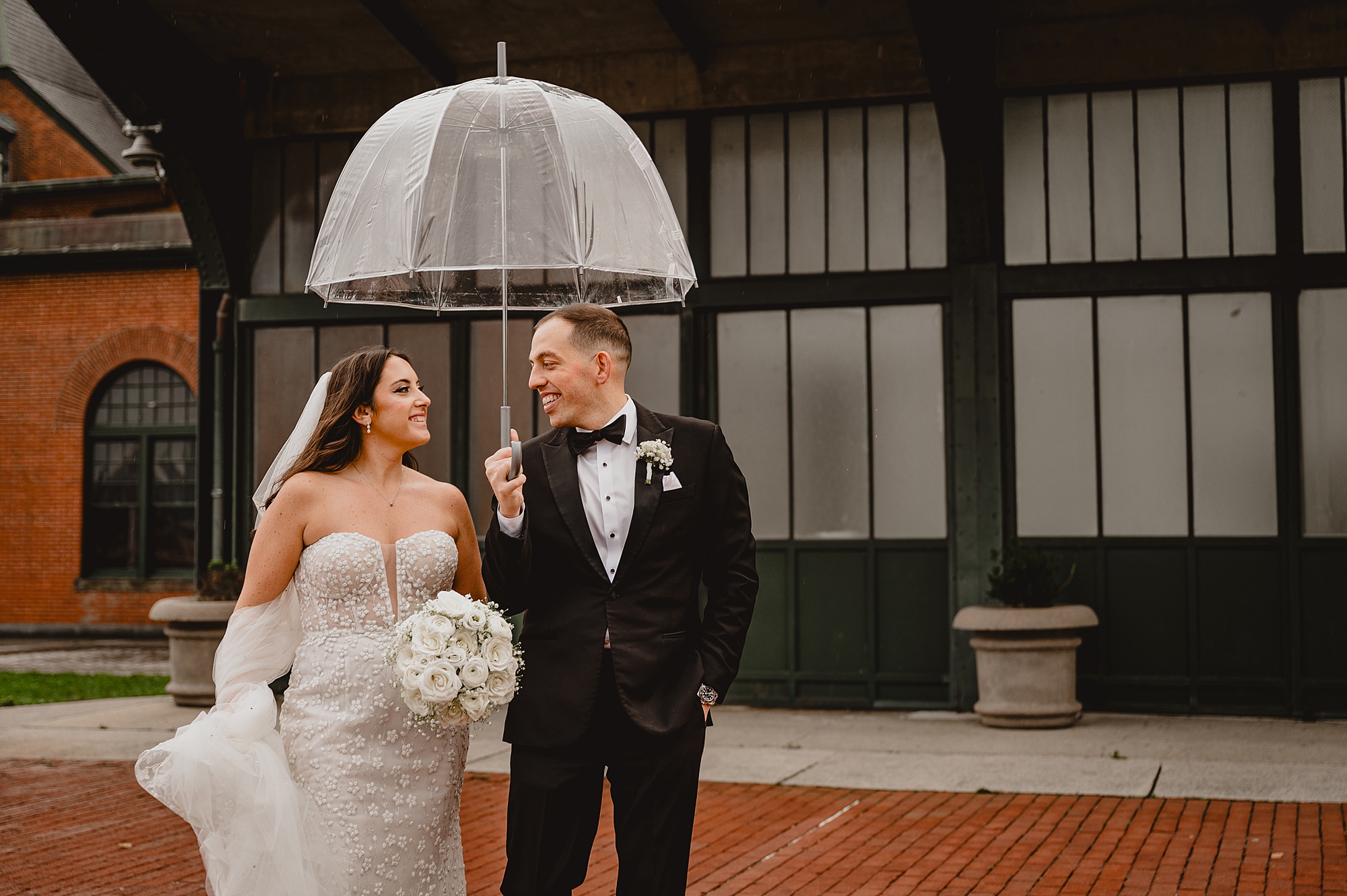 bride and groom walk under clear umbrella on rainy wedding day at the Liberty House